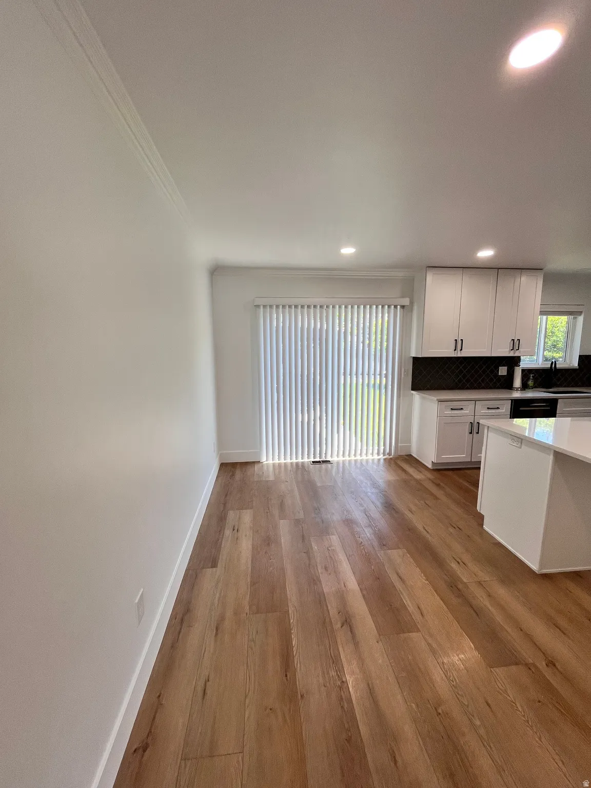 Open-concept living area featuring wood-finish flooring, recessed lighting, and a sliding glass door with vertical blinds
