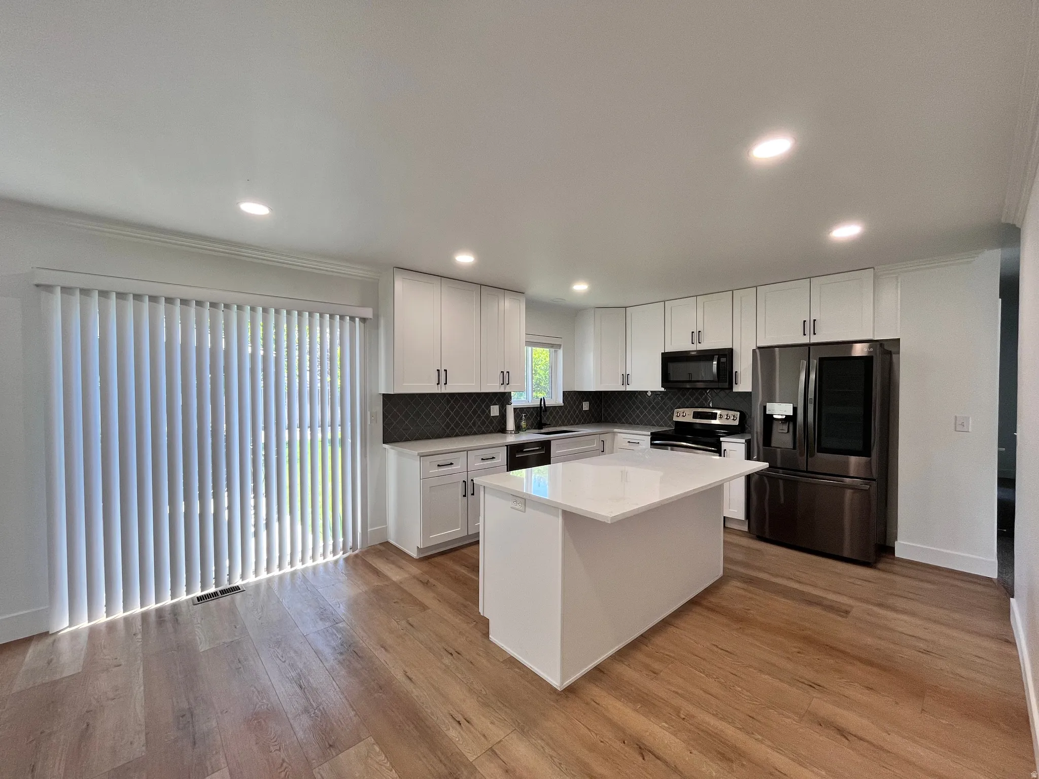Modern kitchen featuring white cabinetry, a central island with a solid surface countertop, dark stainless steel appliances, and wood-finish flooring