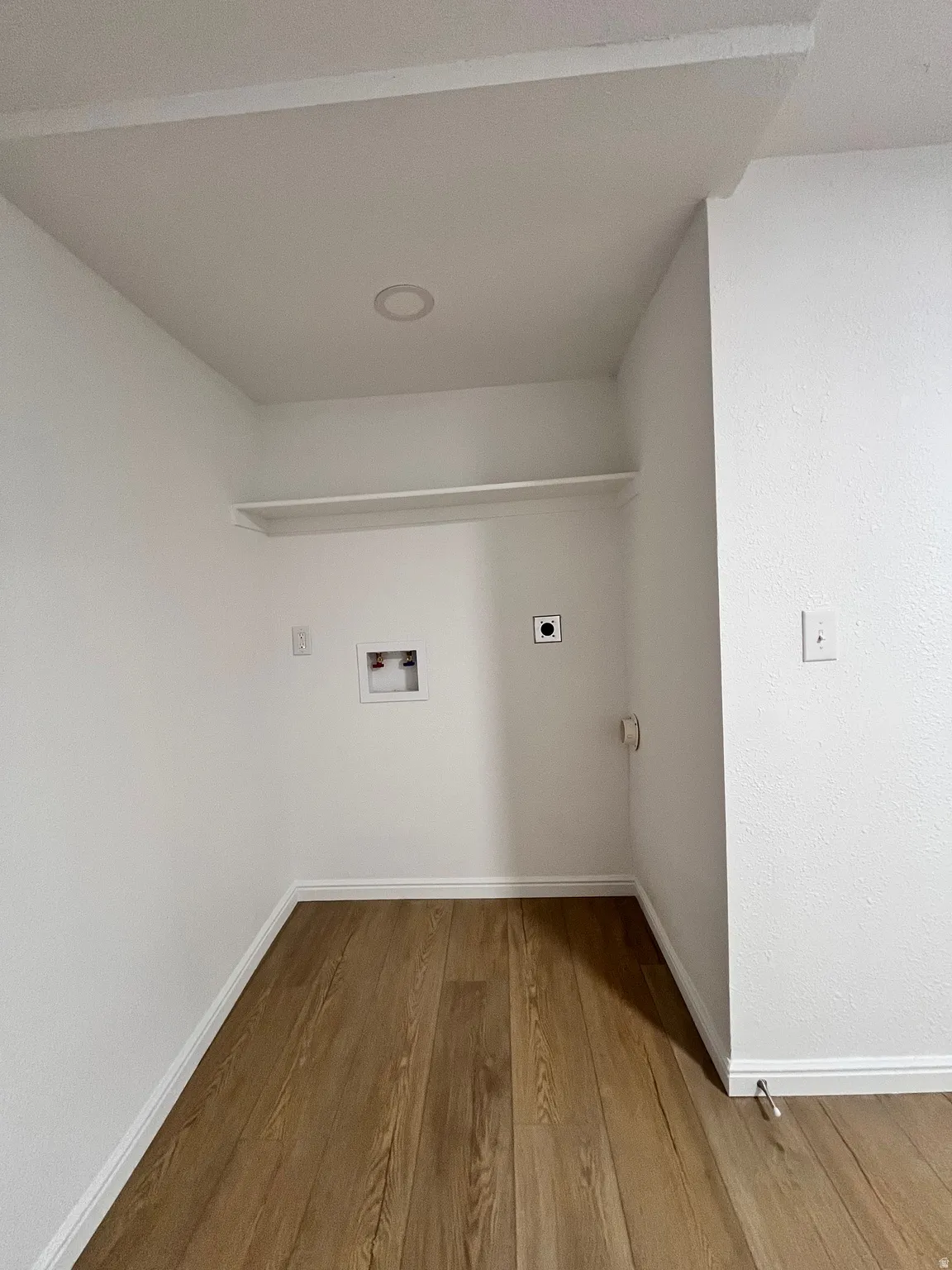 Dedicated laundry area featuring wood-finish flooring, crisp white walls, and a recessed ceiling light