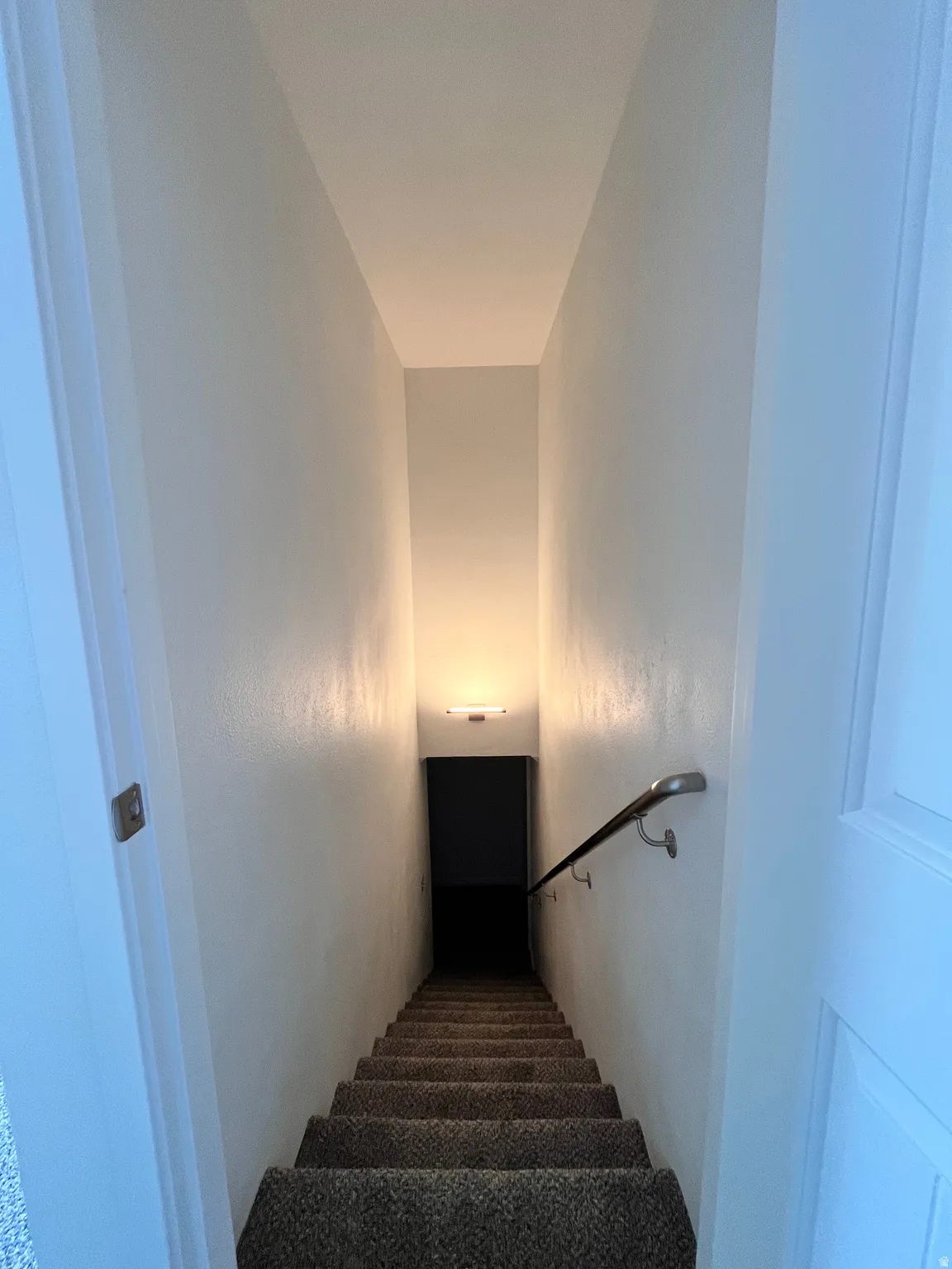 Carpeted staircase featuring a wall-mounted handrail, recessed wall lighting, and painted walls
