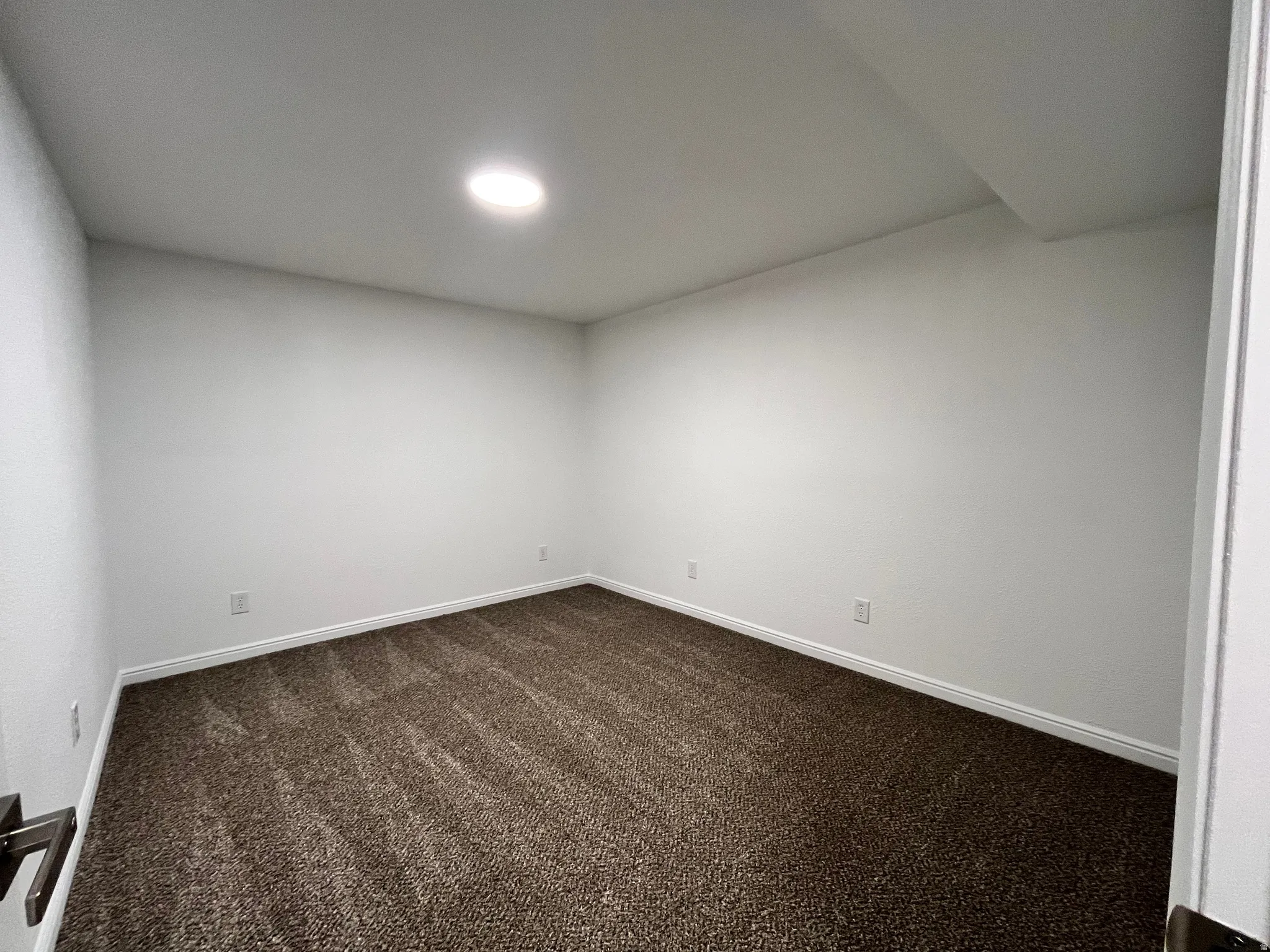 Recessed lighting illuminates this room, featuring light-colored walls, white baseboards, and brown-tone carpeting