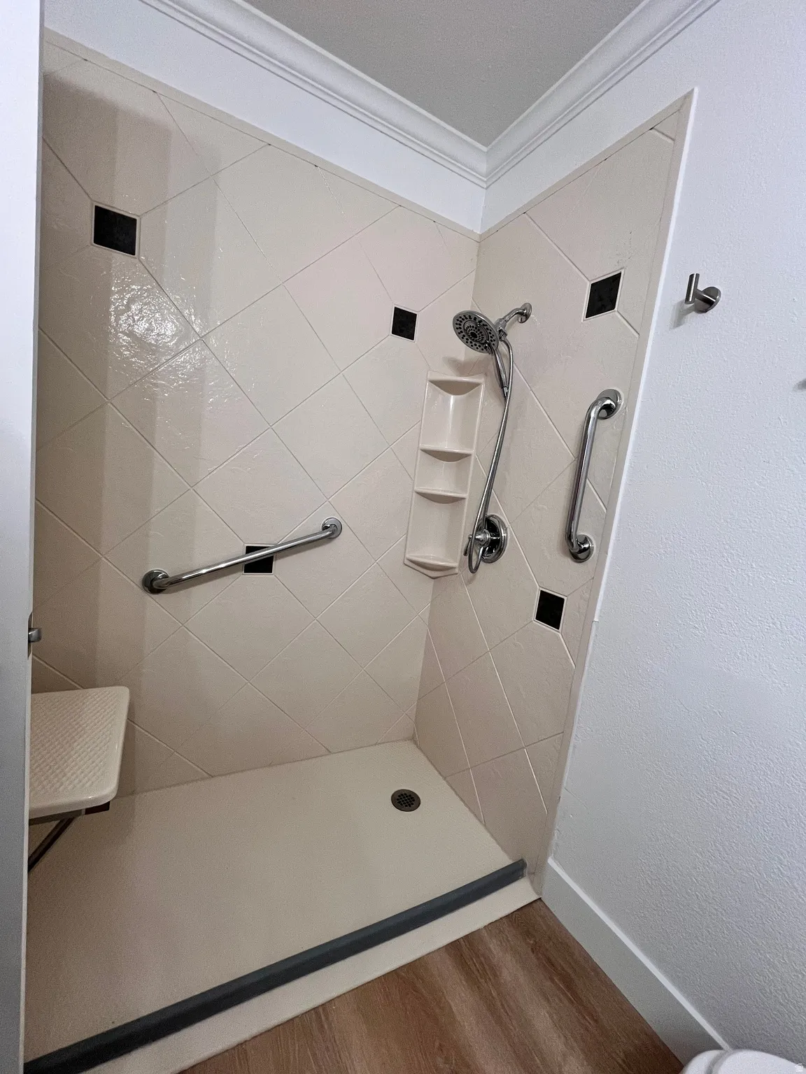 Shower stall with light-toned diagonal tilework featuring black accent tiles, a mounted shower head, a built-in shelving unit, and integrated grab bars