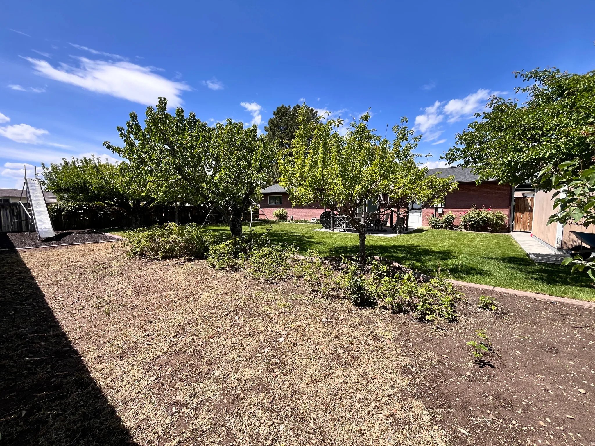 Expansive backyard featuring a green lawn, mature trees, and a red brick exterior on the main residence