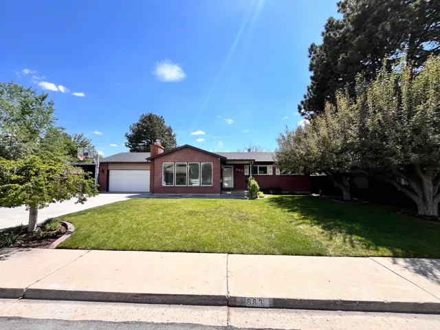 Brick facade residence featuring a two-car garage, expansive front lawn, mature trees, and a concrete driveway