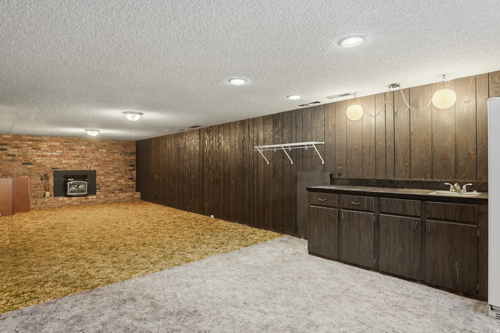 Finished room featuring a brick-clad fireplace, wood paneling, and a built-in wet bar with a sink and dark countertops