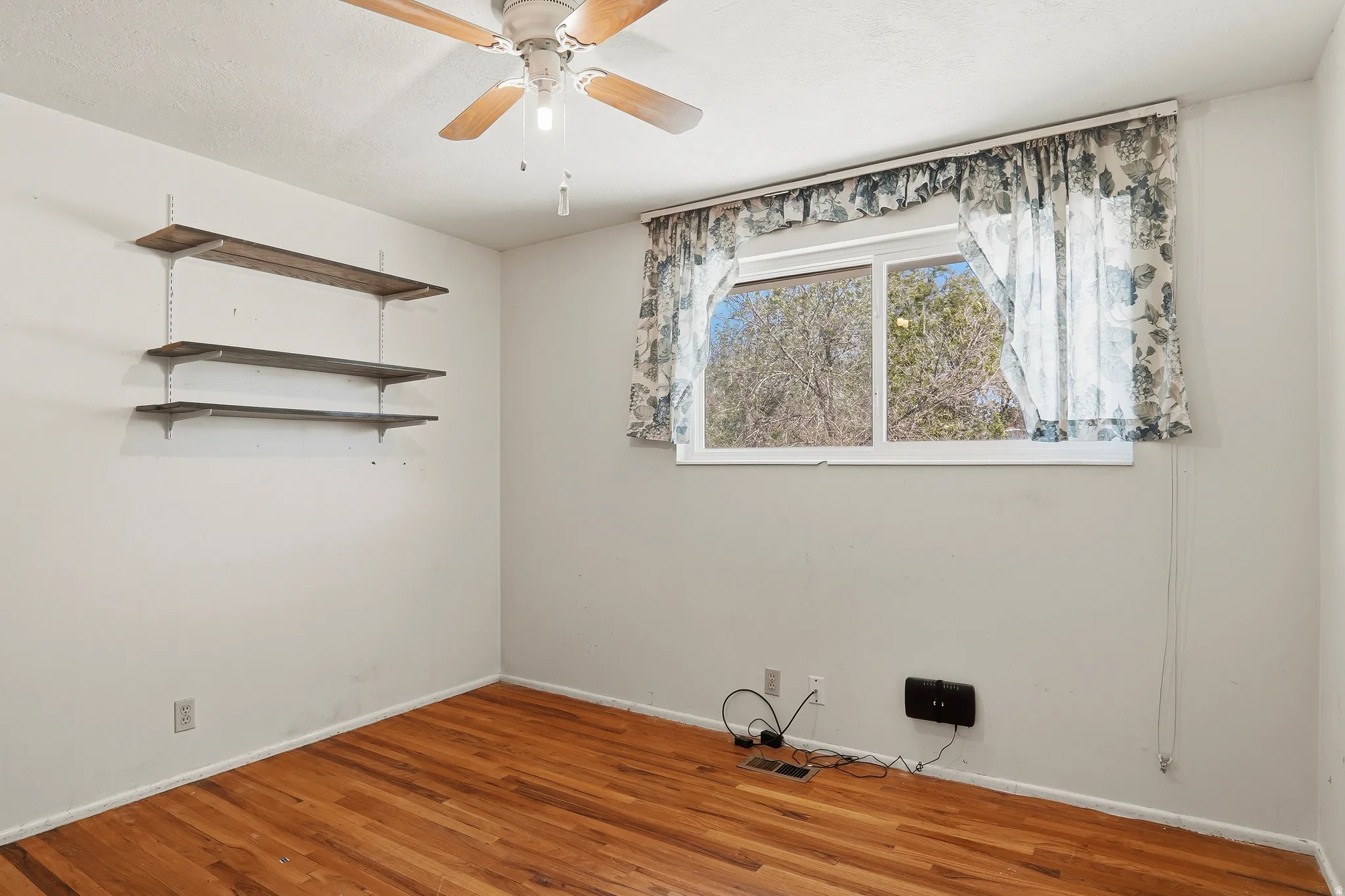 Room featuring wood-finish flooring, a ceiling fan, and built-in shelving