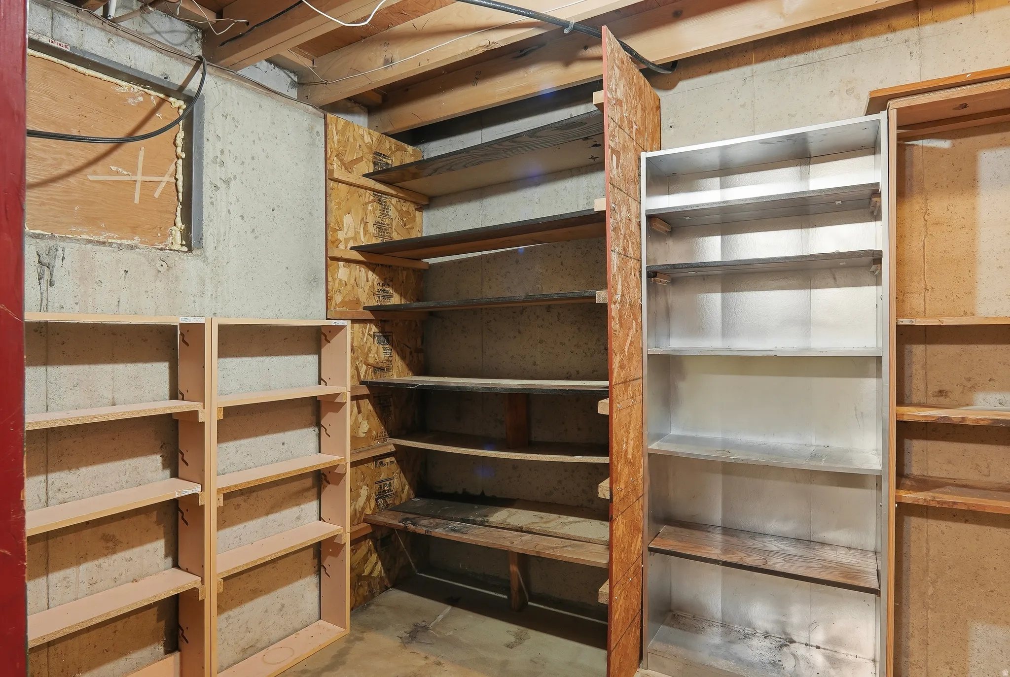 Basement storage area featuring exposed ceiling joists, concrete walls, and a combination of wood and metal shelving units