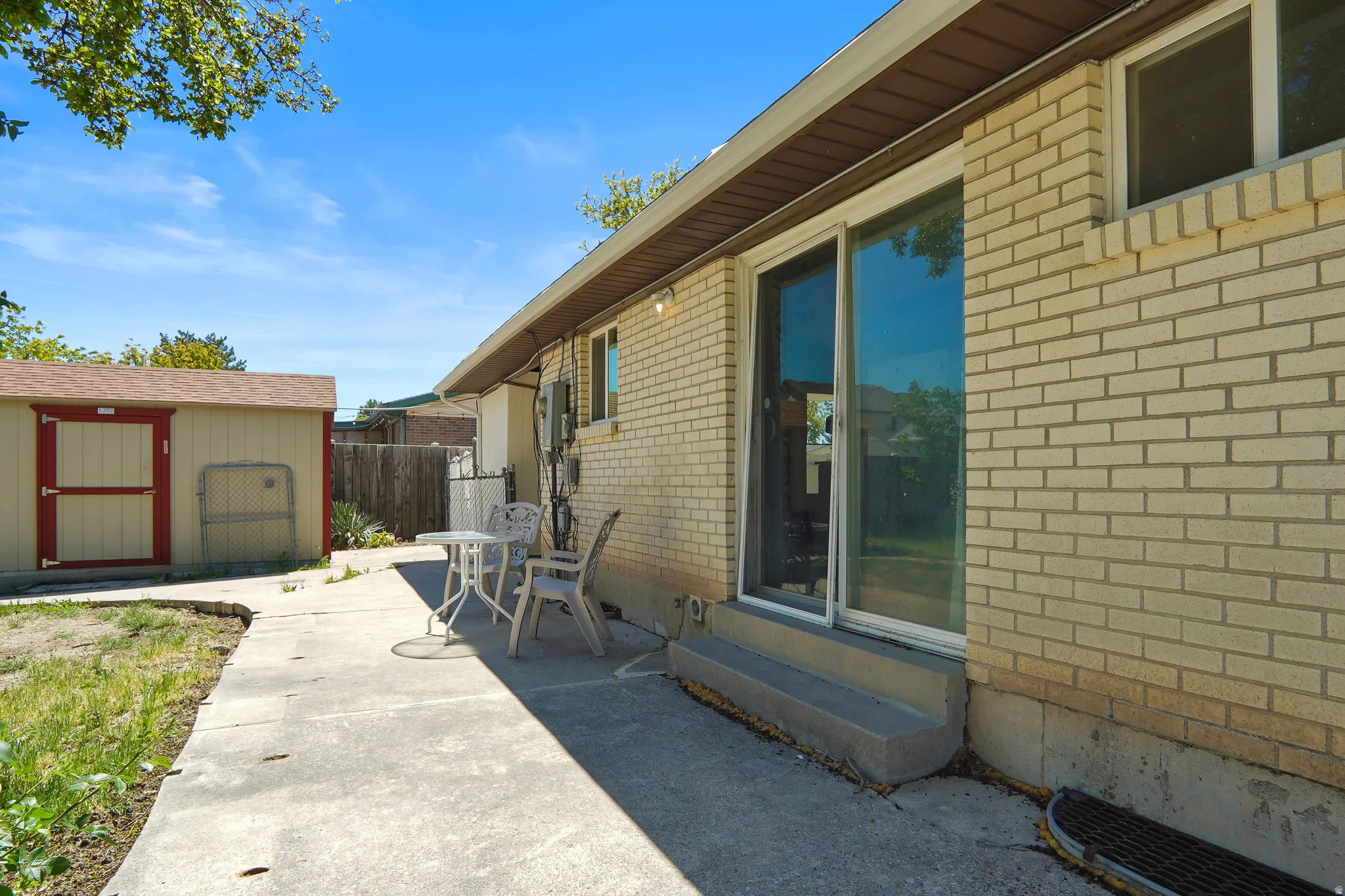 Brick exterior with sliding glass door access to a concrete patio, featuring an included shed and partial fencing