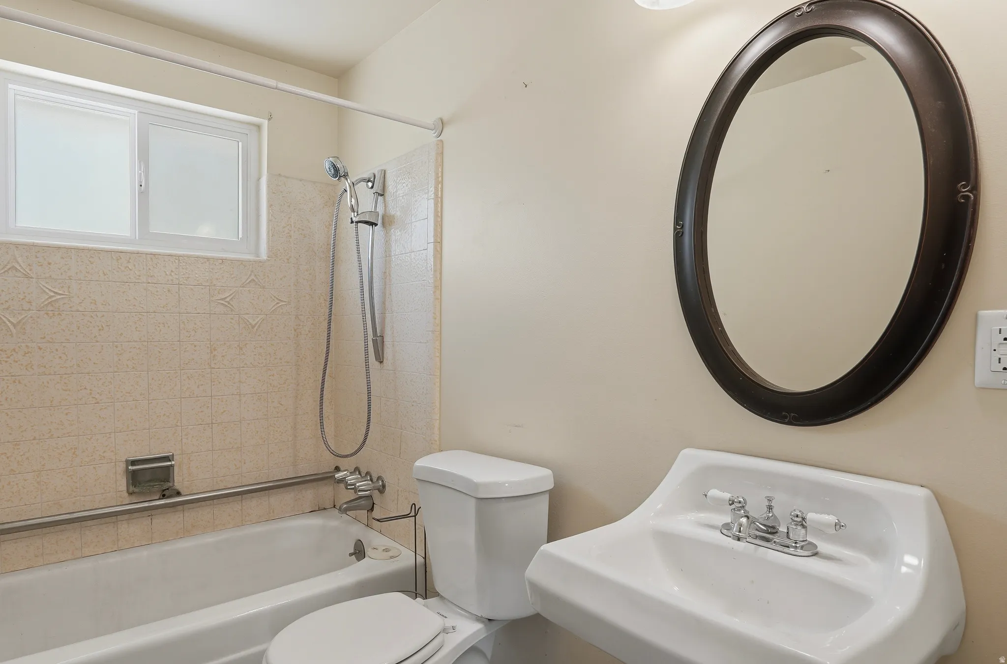 Full bathroom featuring a pedestal sink, oval framed mirror, and a tub with a shower fixture