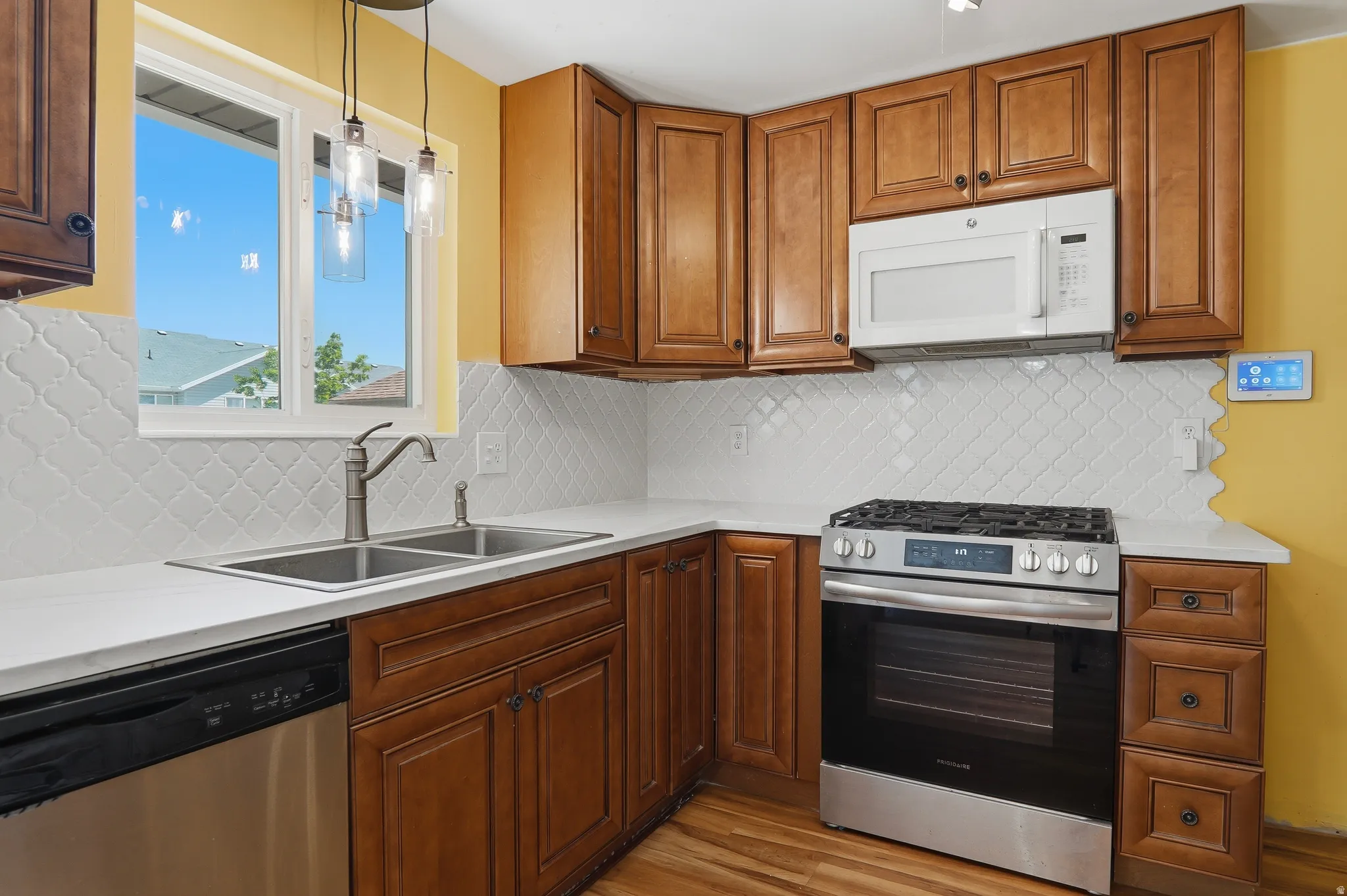 Kitchen featuring wood-finish cabinetry, white countertops, a white patterned tile backsplash, stainless steel appliances, and a double basin sink with a gooseneck faucet