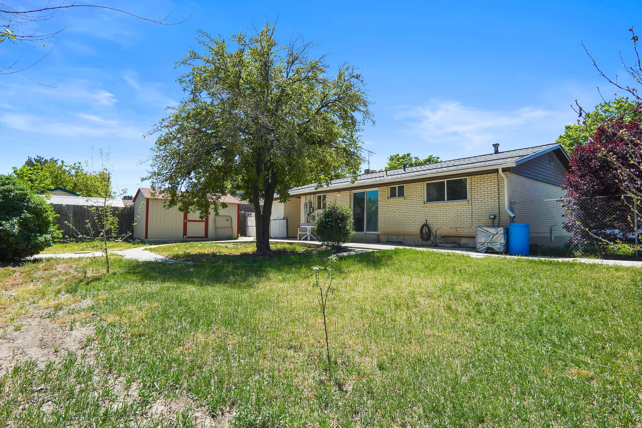 Expansive backyard featuring a mature tree, a detached storage shed, and a brick exterior home with sliding glass doors
