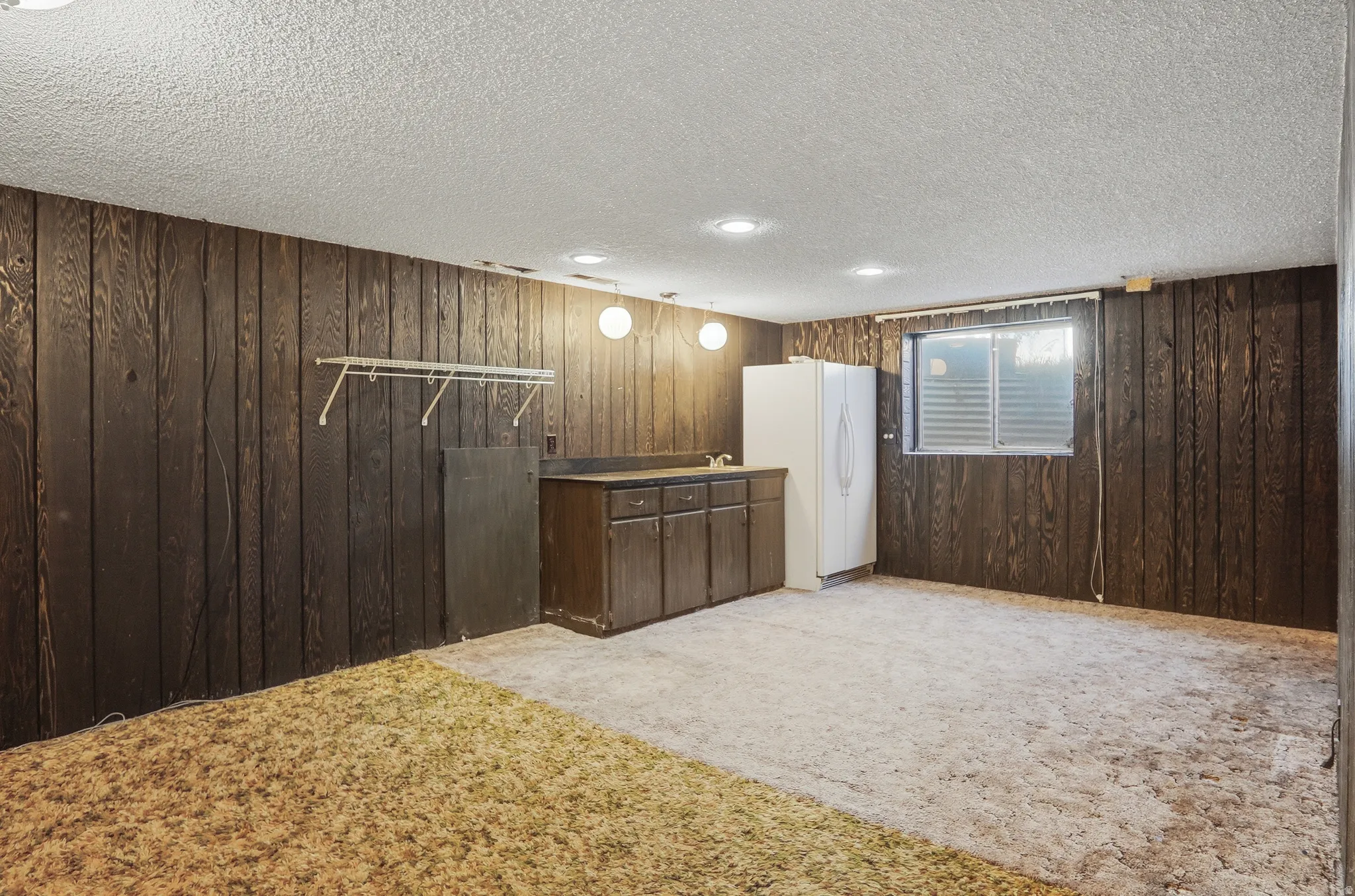 Finished space featuring wood-paneled walls, a built-in wet bar with cabinetry, a window with horizontal blinds, and a combination of wall-mounted and recessed lighting