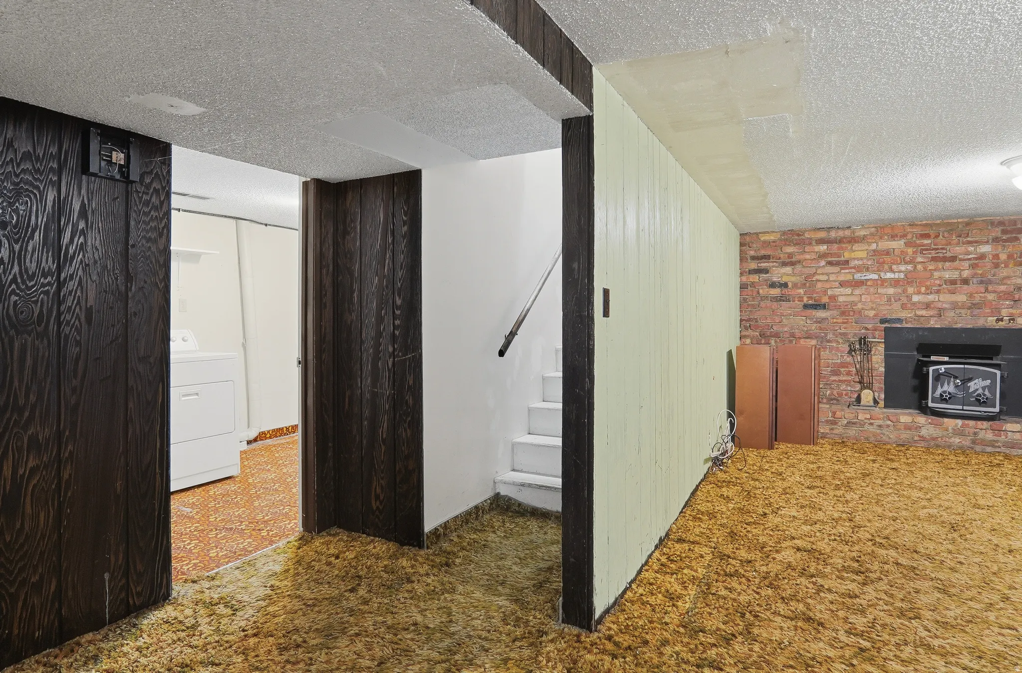 Lower-level space featuring a brick fireplace with a black insert, wood-panel accent wall, and textured ceiling