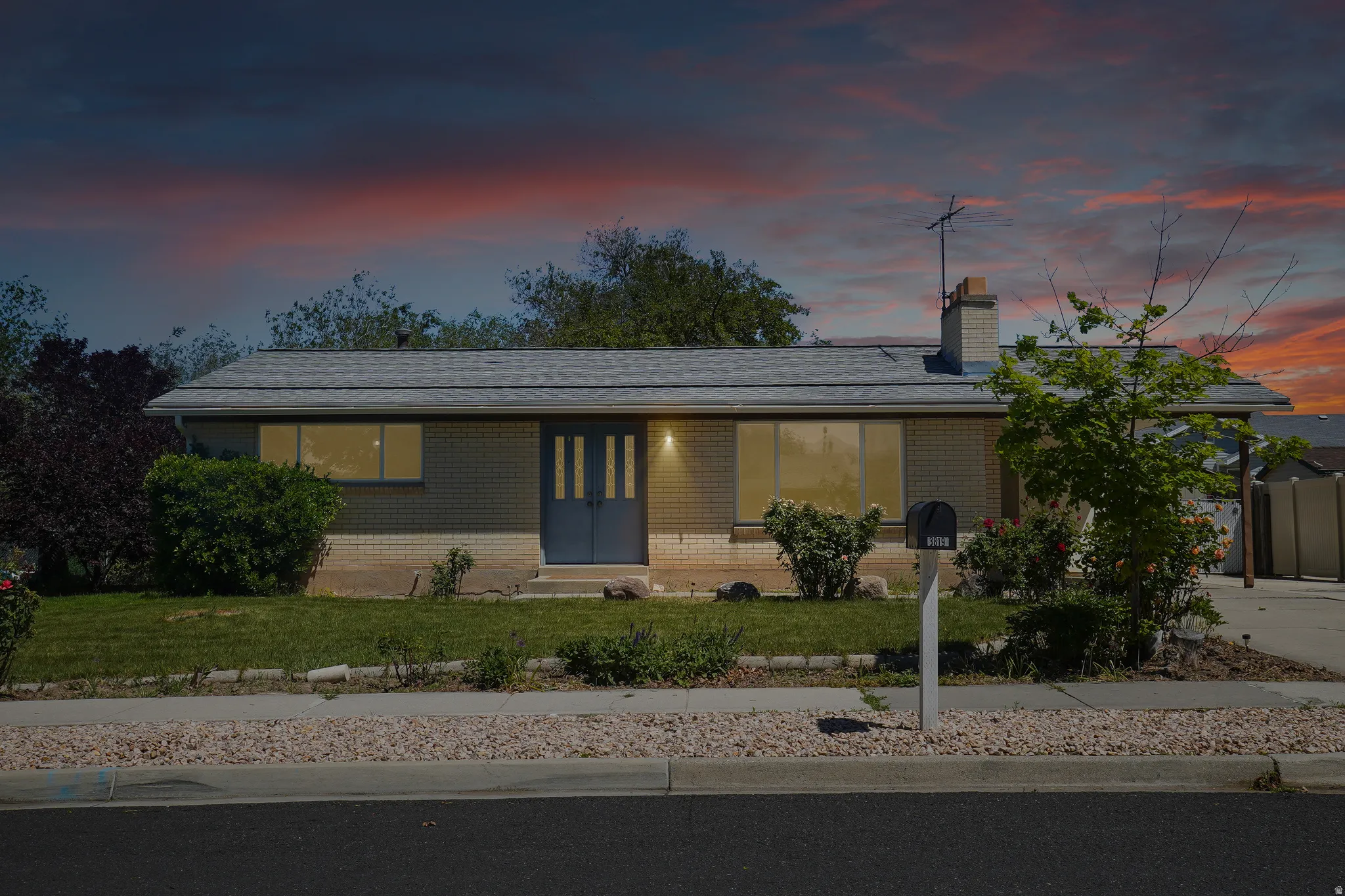 Ranch-style residence featuring a brick facade, dual entry doors, a gray shingle roof, and a mature landscaped front yard