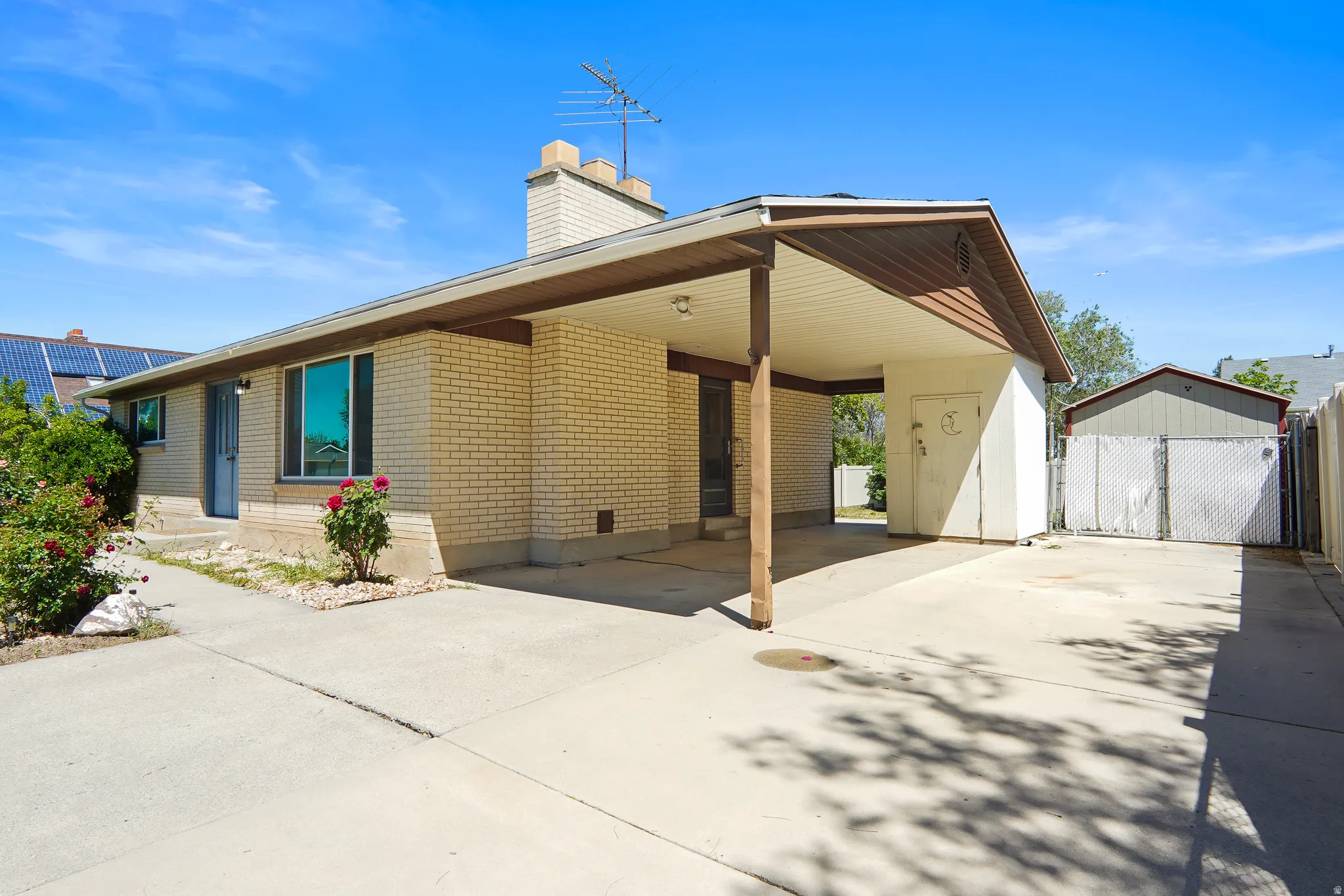 Exterior featuring a brick facade, covered carport, concrete driveway, and an additional shed structure