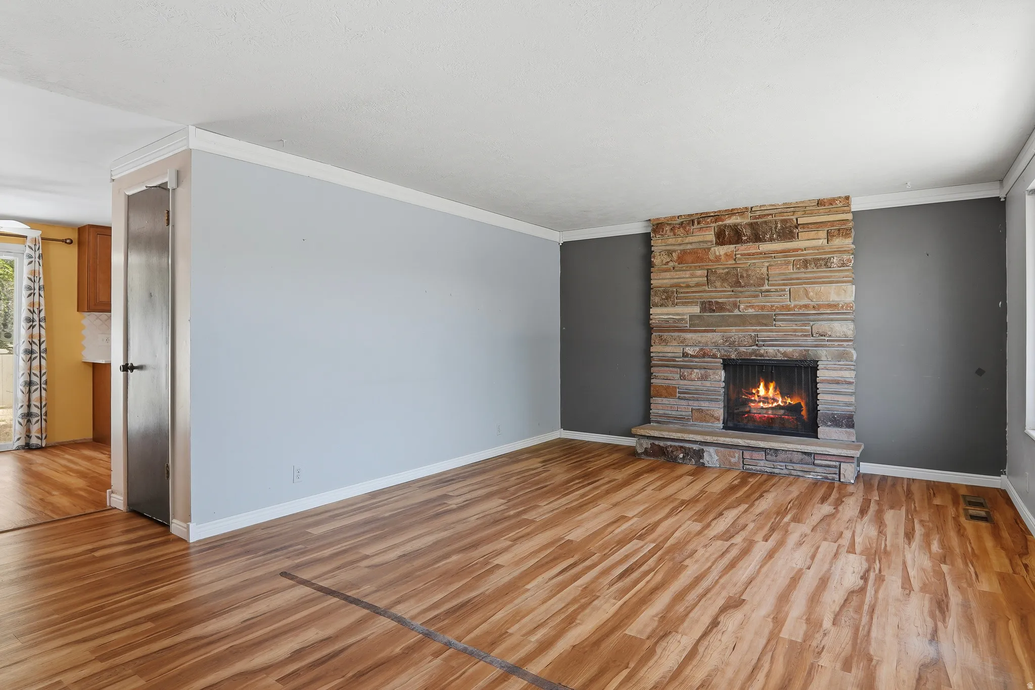 Living area featuring a floor-to-ceiling stone fireplace, wood-finish flooring, and crown molding