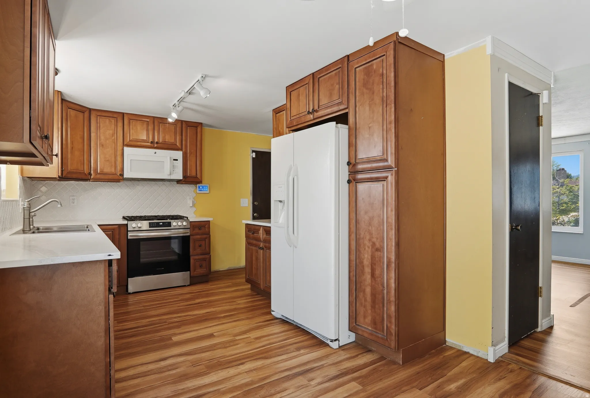 Kitchen featuring wood-finish flooring, wood cabinetry, white countertops, and a subway tile backsplash