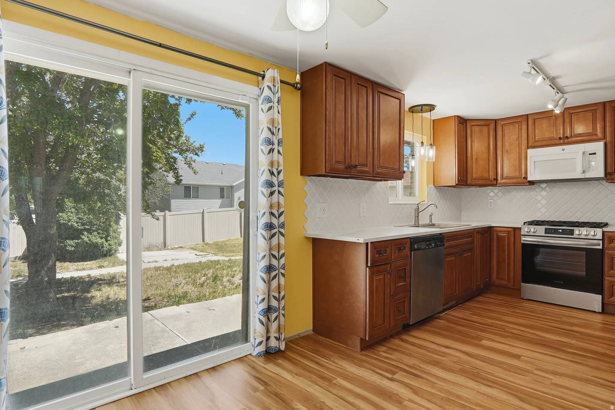 Kitchen featuring wood-finish flooring, warm-toned cabinetry, light countertops, and a white geometric tile backsplash