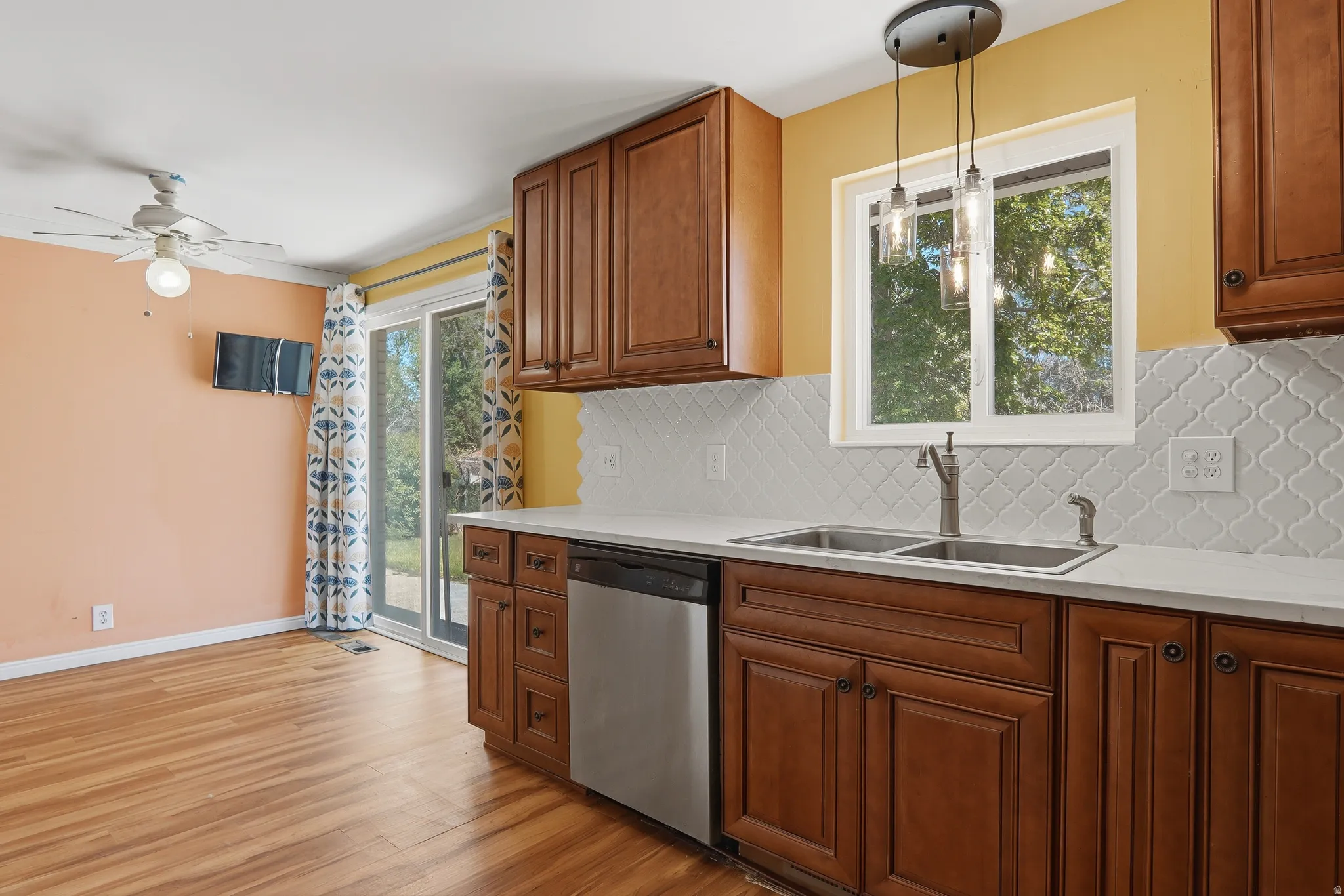 Kitchen featuring wood-finish flooring, cherry-toned cabinetry, stainless steel sink, white countertop, and patterned white tile backsplash