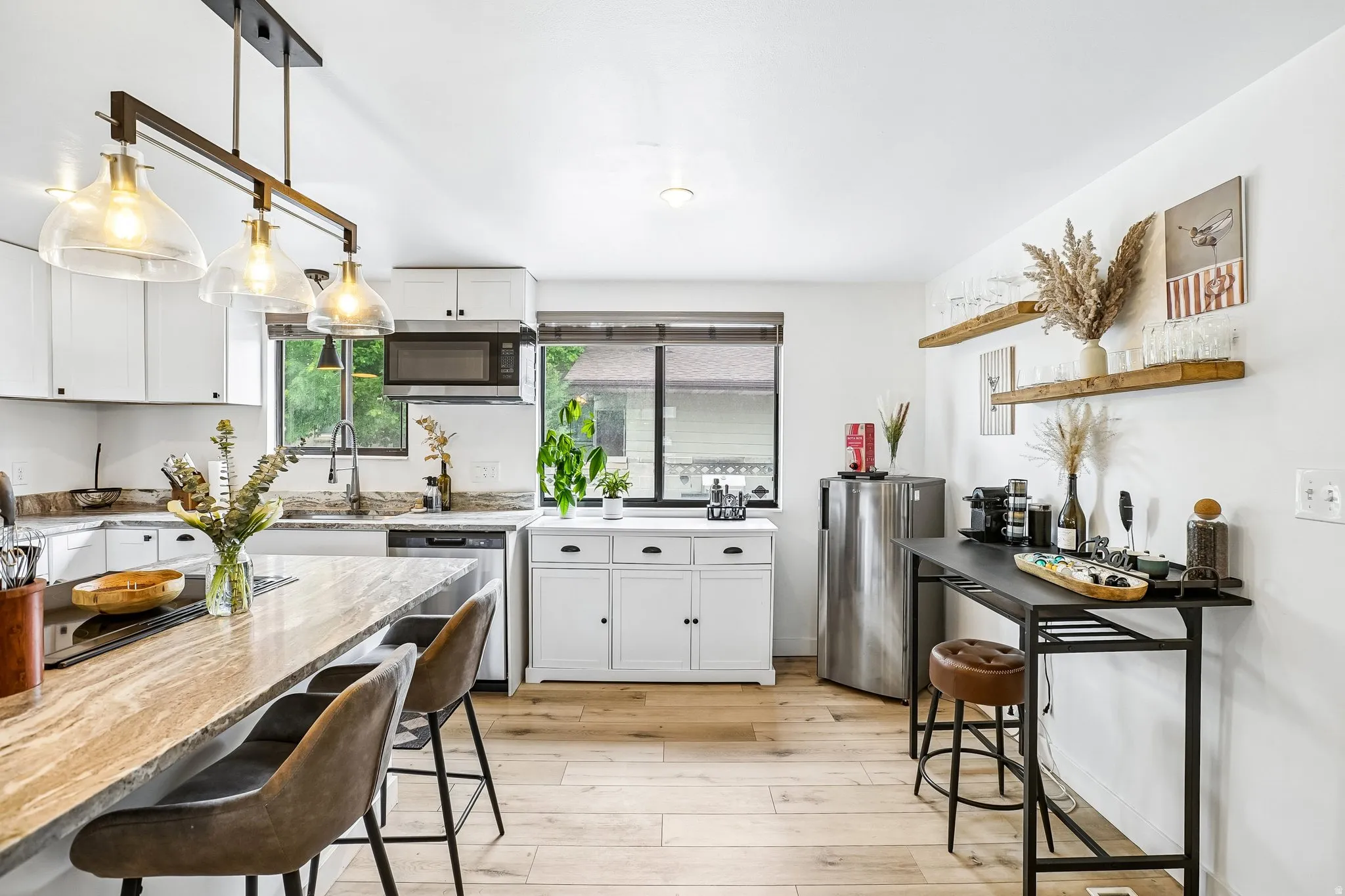 Open-concept kitchen featuring an island with a light-toned countertop, white cabinetry, integrated stainless steel appliances, pendant lighting, and wood-finish flooring