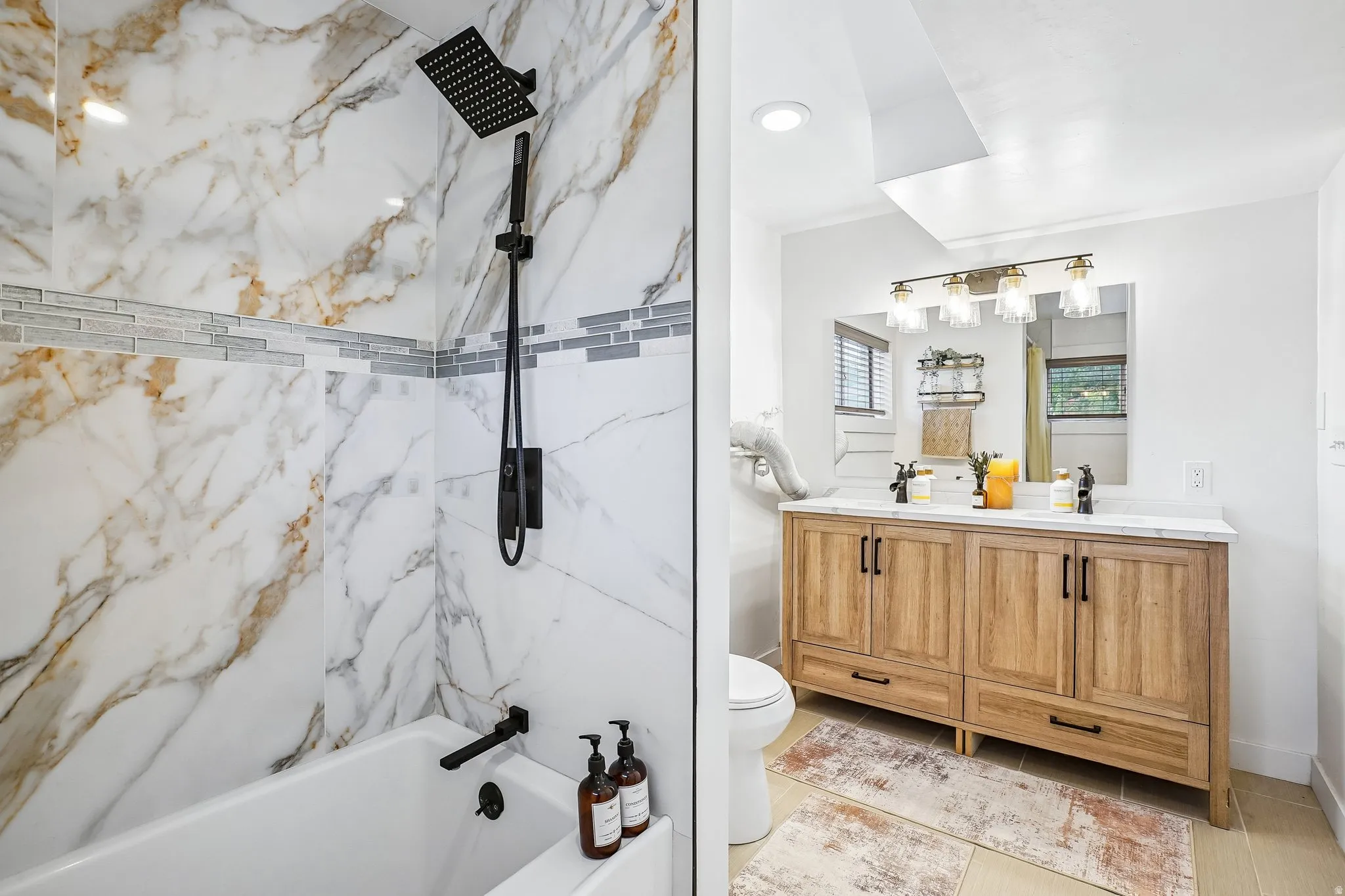 Bathtub and shower combination featuring black matte fixtures, marble-look wall tiling with a decorative mosaic accent, and a handheld shower head