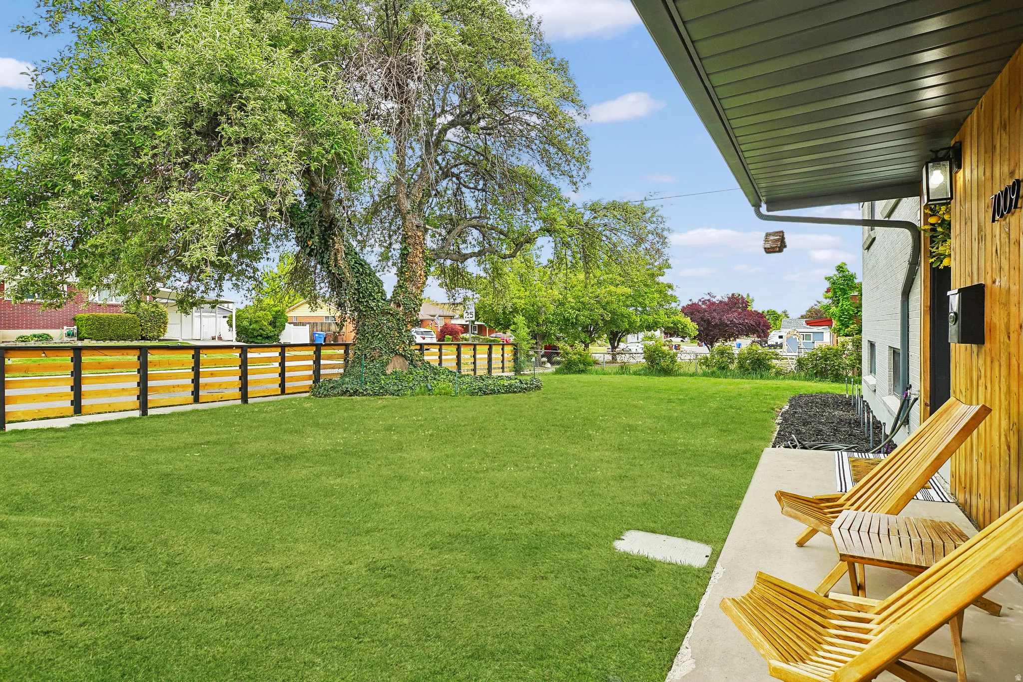 Expansive front lawn featuring mature trees and a horizontal slat fence
