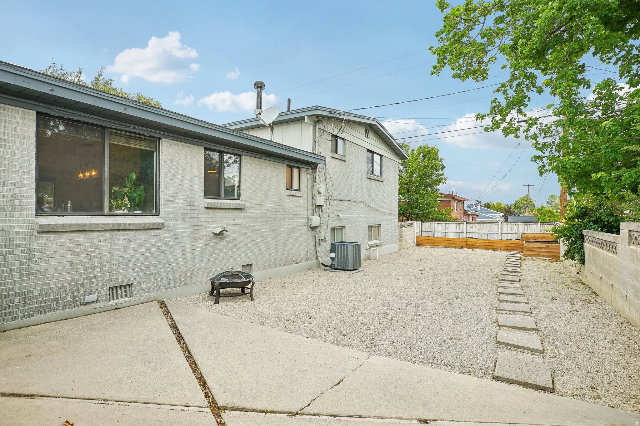 Expansive gravel backyard featuring concrete stepping stones, a wooden retaining wall, and mature perimeter trees