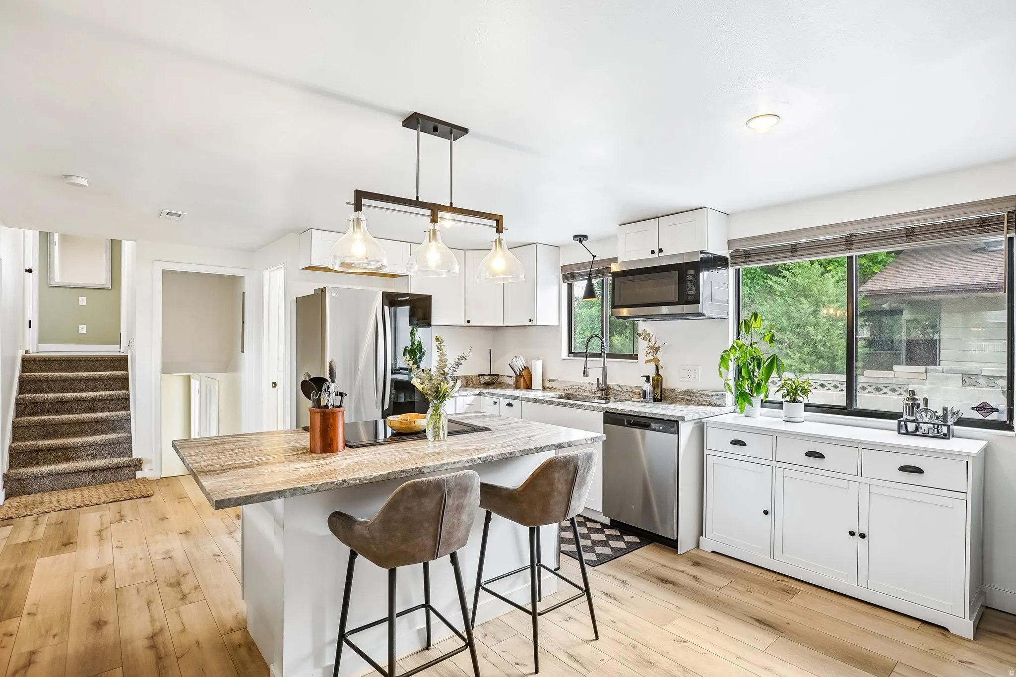 Kitchen featuring an island with stone countertop, wood-finish flooring, white cabinetry, stainless steel appliances, and a large window