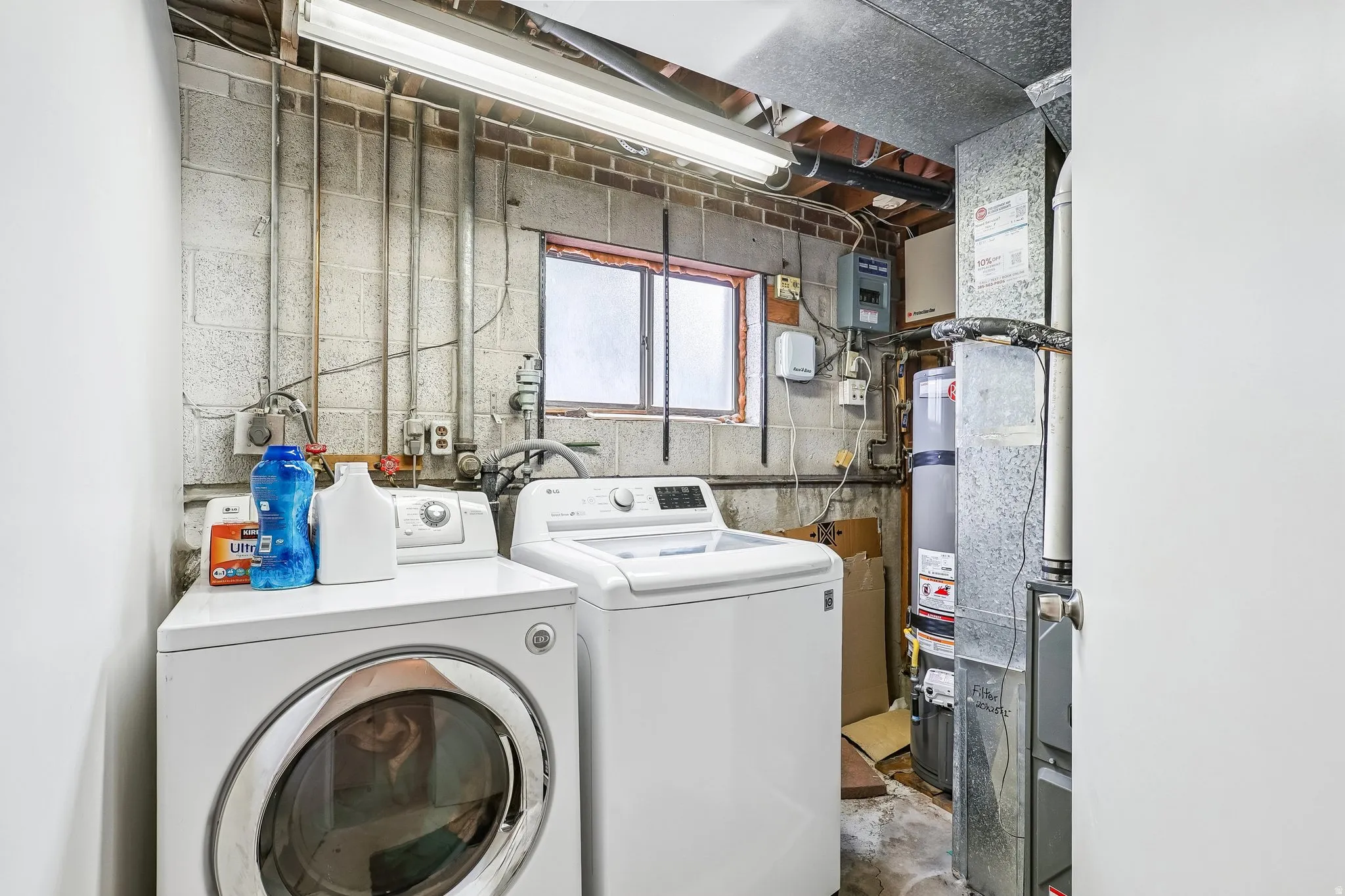 Dedicated utility space featuring concrete block walls, exposed piping, and a window for natural light