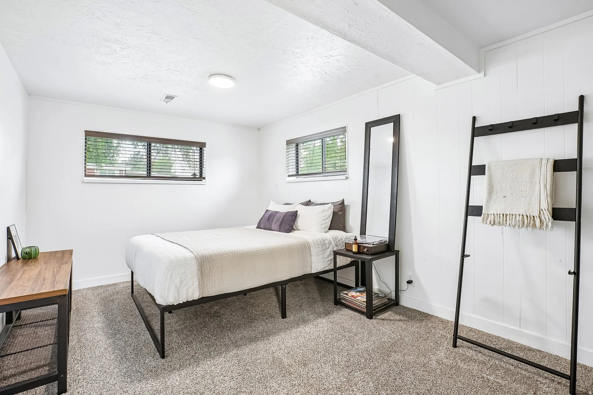 Carpeted room featuring two windows with horizontal blinds, white walls, and a white plank accent wall