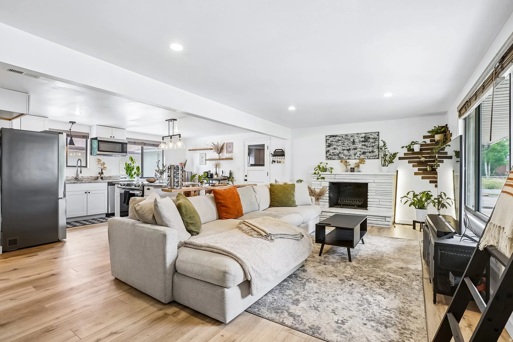 Open-concept living space featuring wood-finish flooring, a stone-surround fireplace, and large windows