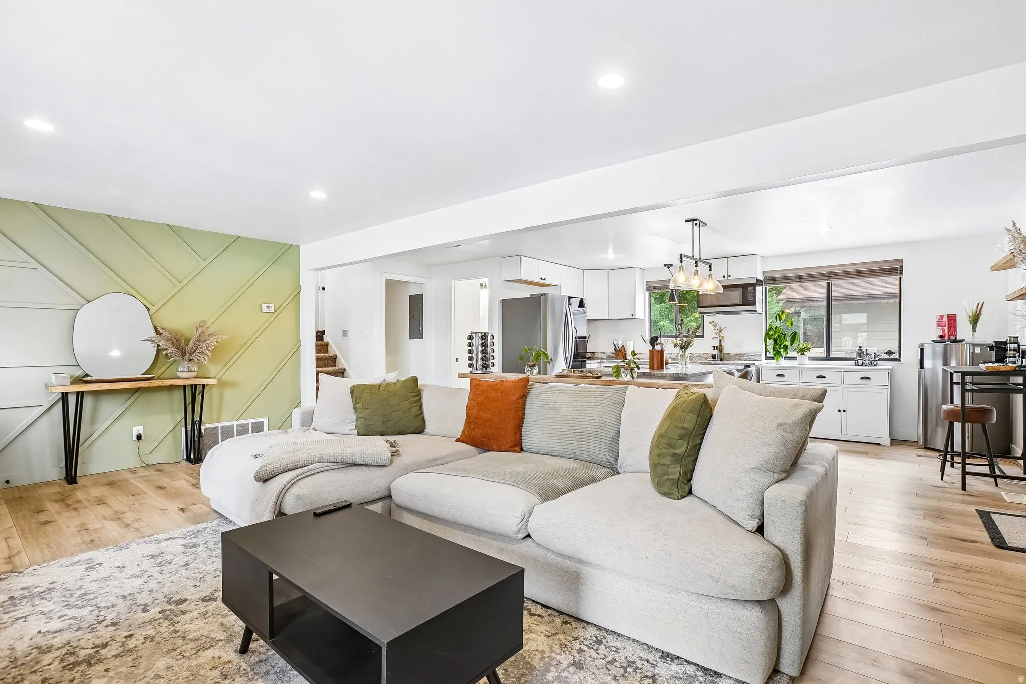 Open-concept living space featuring wood-finish flooring, a decorative accent wall with a geometric pattern, recessed lighting, white cabinetry, and a kitchen island with pendant lighting