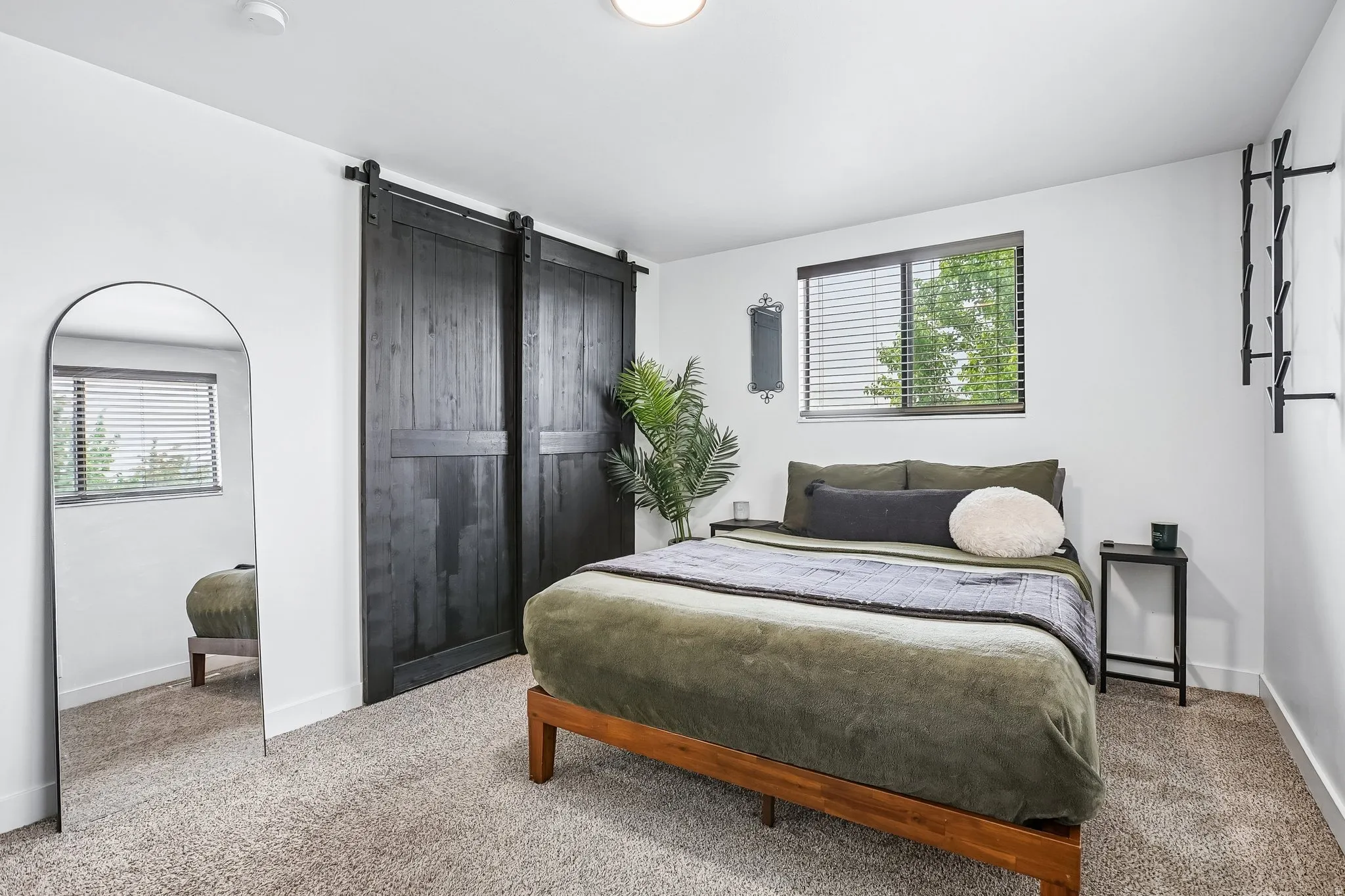 Room featuring two dark wood barn doors with black hardware, a window with horizontal blinds, and light-colored carpet flooring