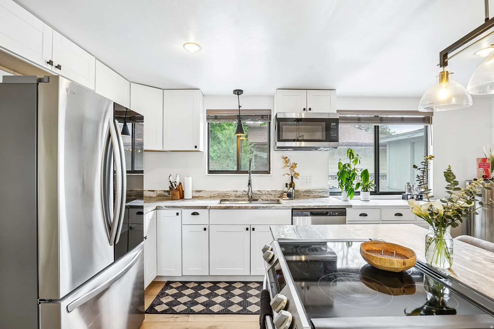 Bright kitchen featuring white cabinetry, stainless steel appliances, light-toned countertops, and wood-finish flooring
