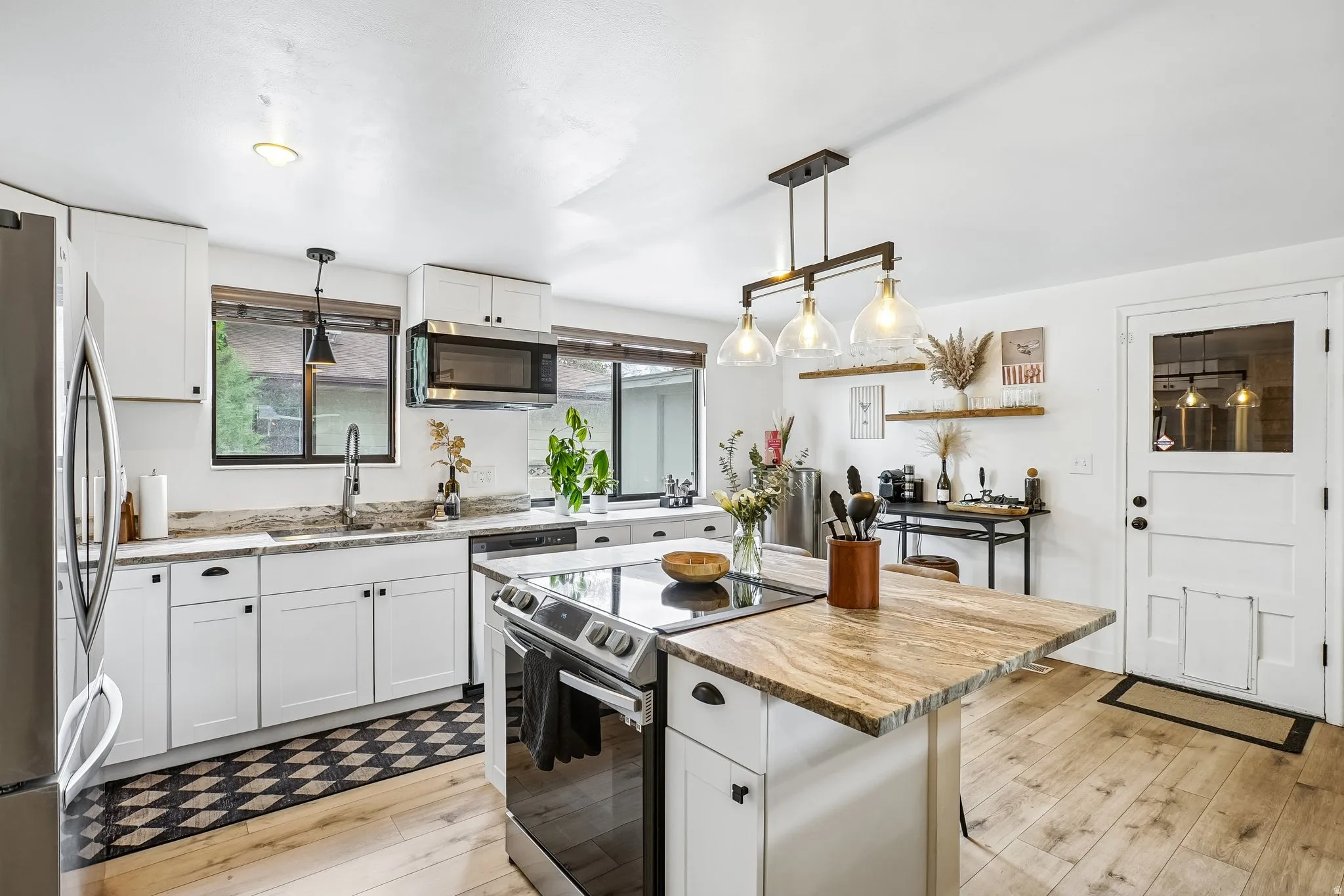 Open-concept kitchen featuring wood-finish flooring, white cabinetry with black hardware, and a center island with a stone countertop