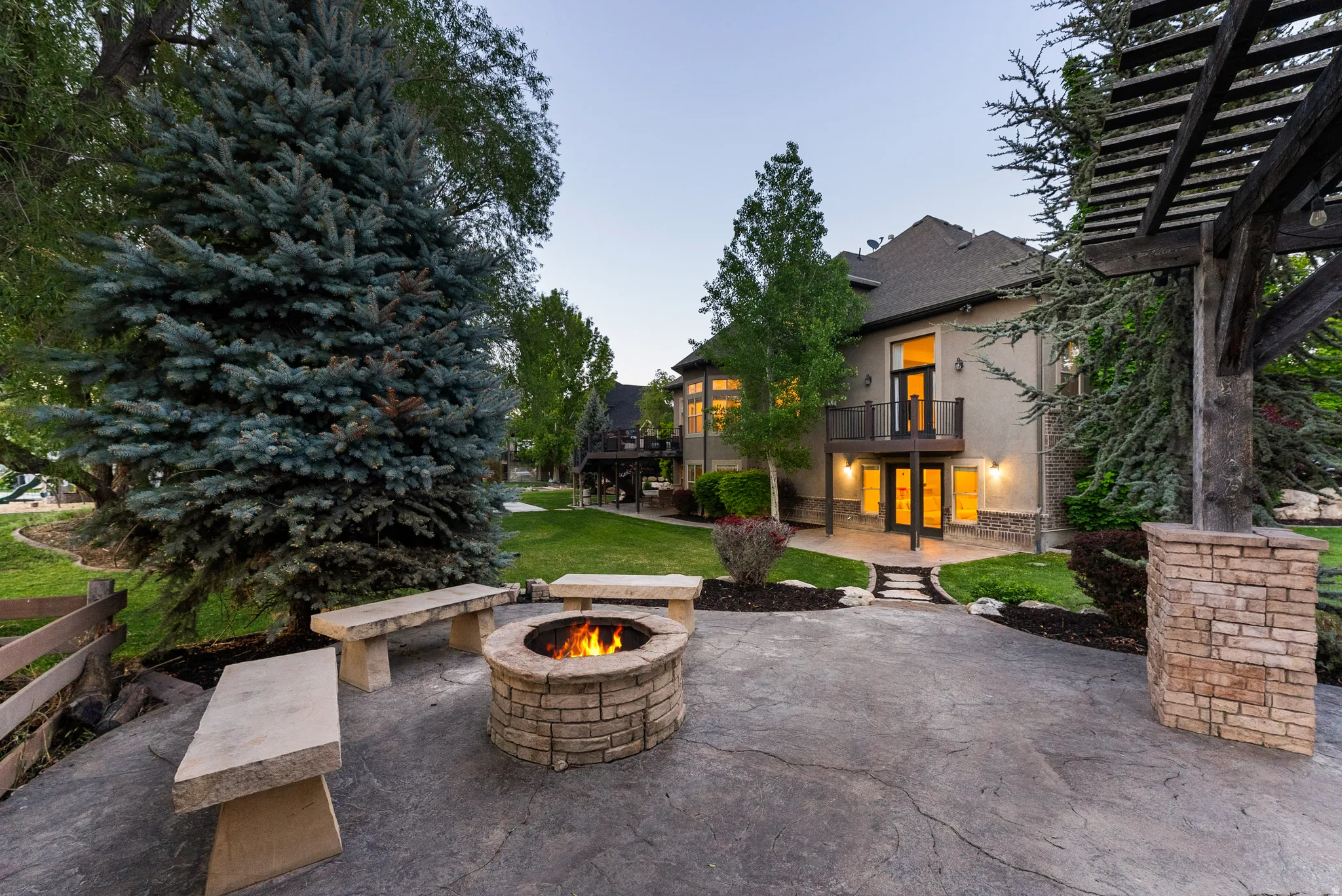 Stained concrete patio featuring a stone fire pit, three stone benches, and a large pergola structure