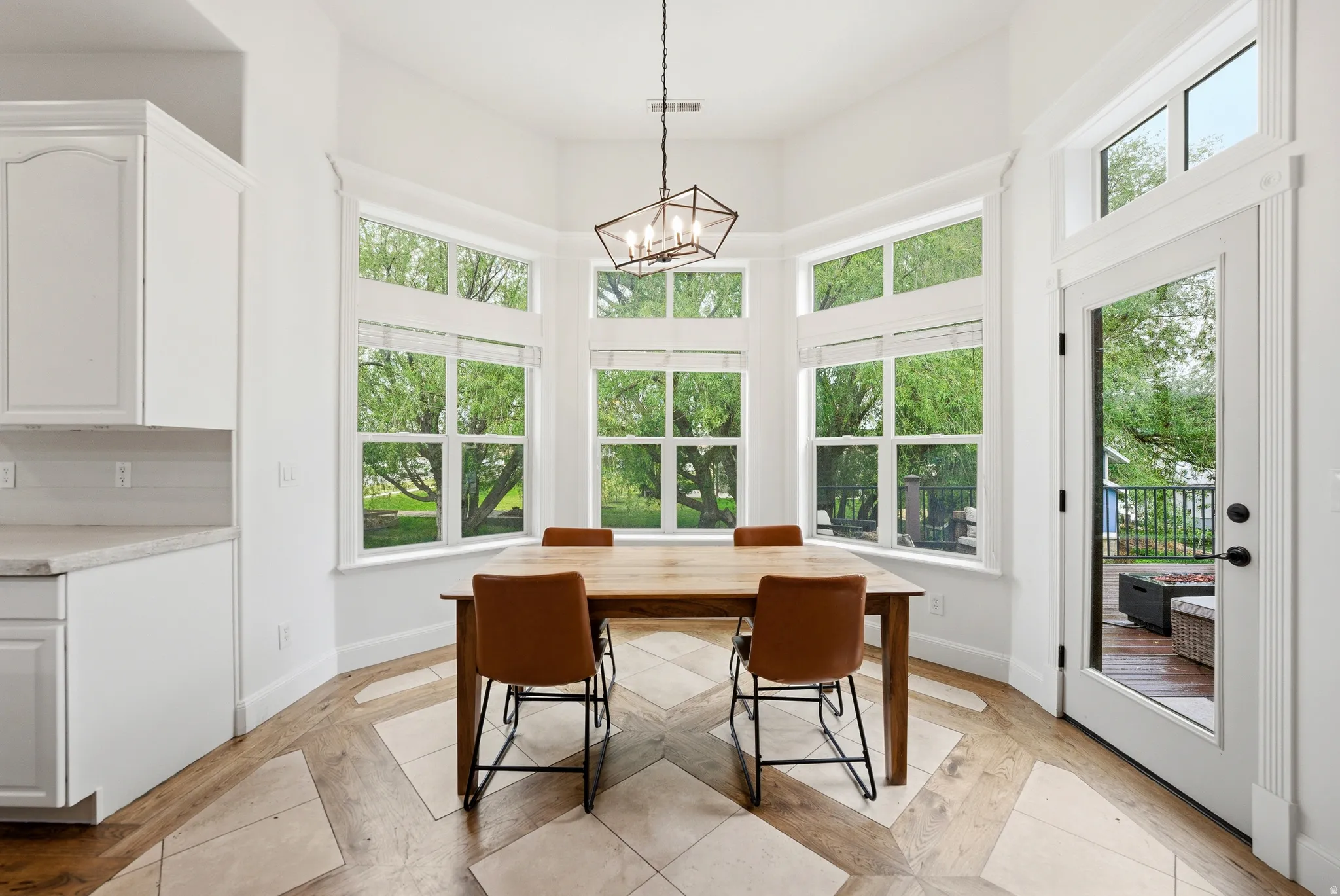 Bay window dining area with pattern wood-finish flooring, white cabinetry, light-toned countertop, and outdoor deck access