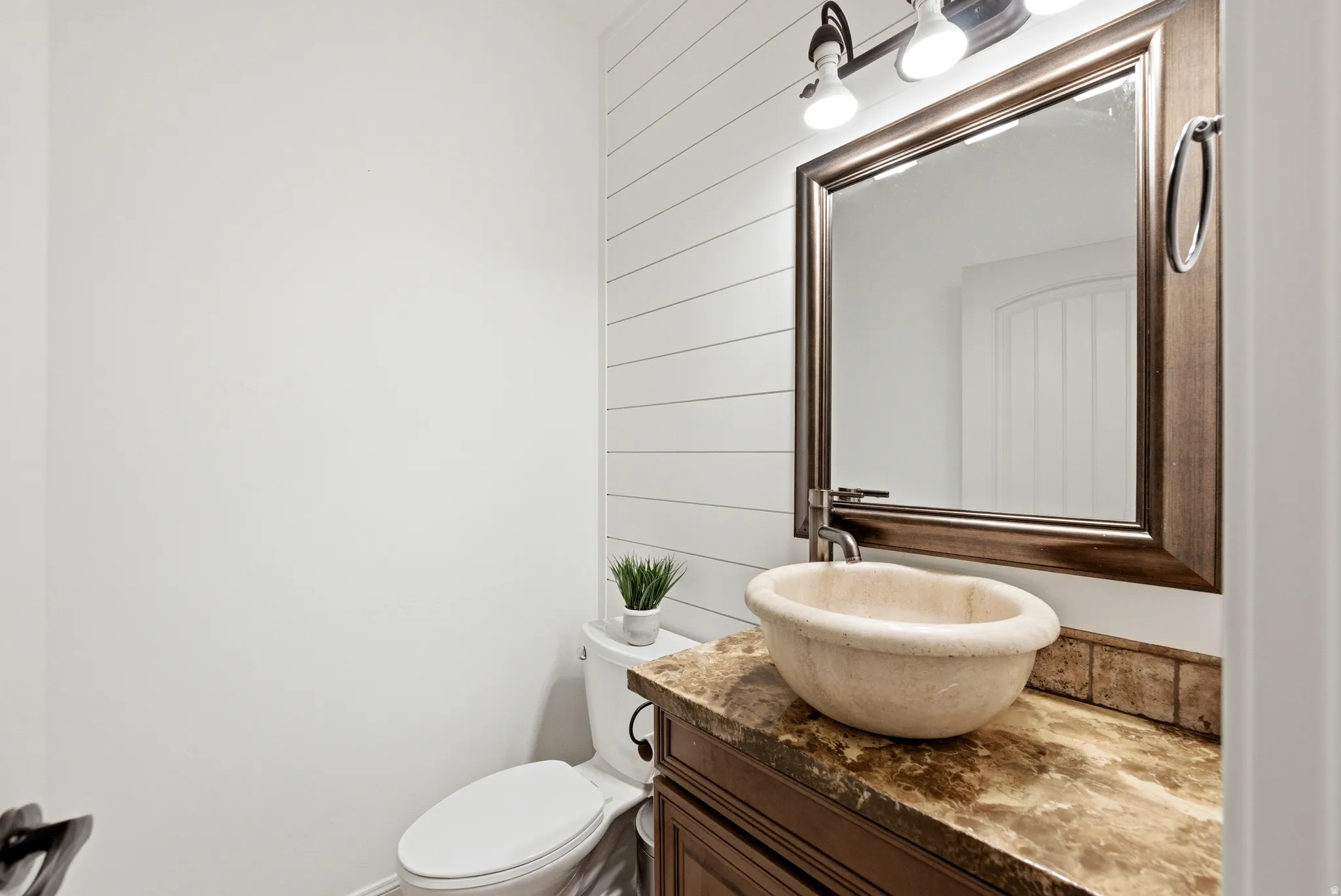 Shiplap accent wall featuring a vessel sink on a stone countertop, framed mirror, and vanity lighting
