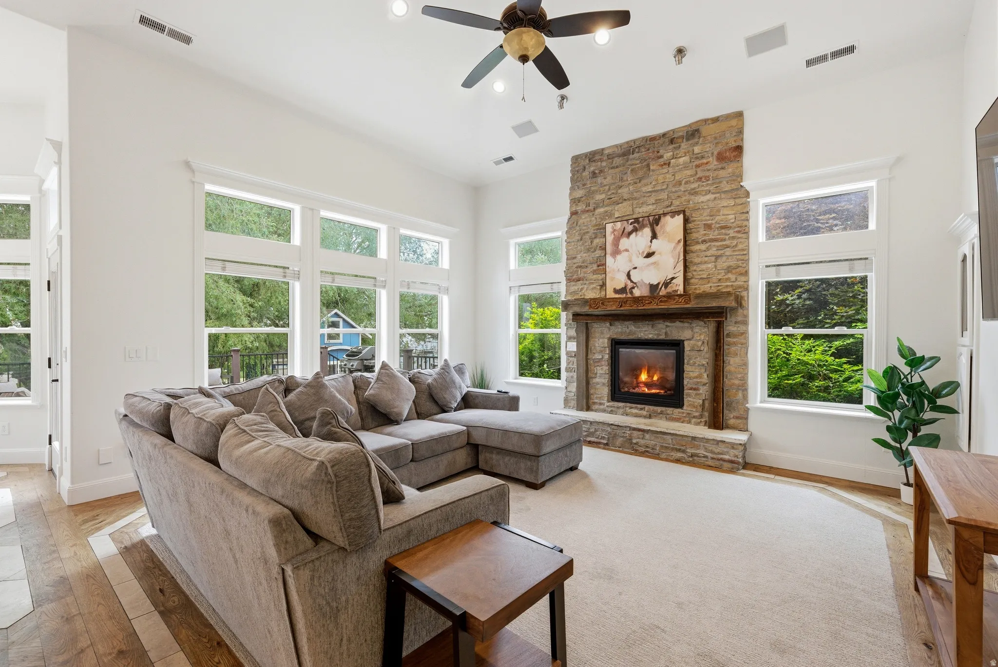Spacious living area featuring a stone-clad fireplace with a wood mantel, high ceilings, multiple large windows, a ceiling fan, and recessed lighting