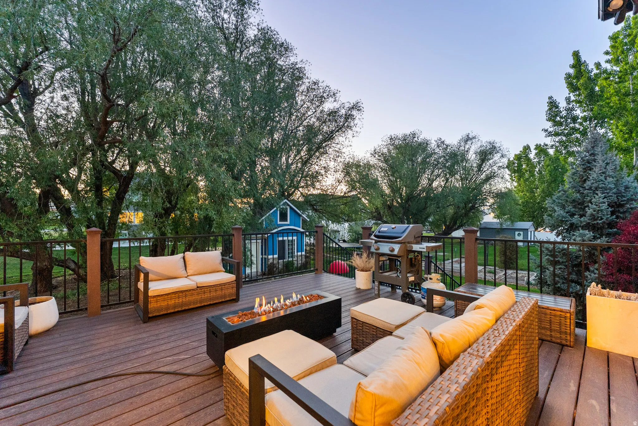 Spacious outdoor deck featuring composite decking, black metal railings, a built-in fire pit, and mature perimeter trees