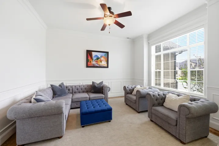 Spacious living area featuring extensive wainscoting, crown molding, and a ceiling fan with integrated lighting
