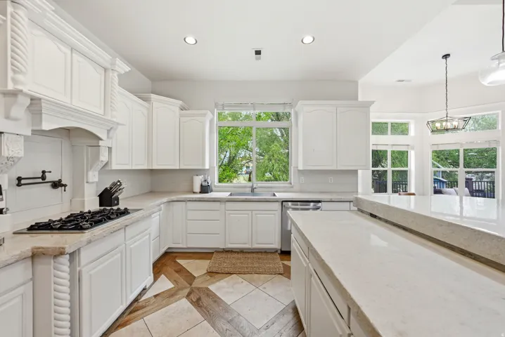 Kitchen featuring white cabinetry, light-toned countertops, a built-in gas range, a pot filler, and a large central island