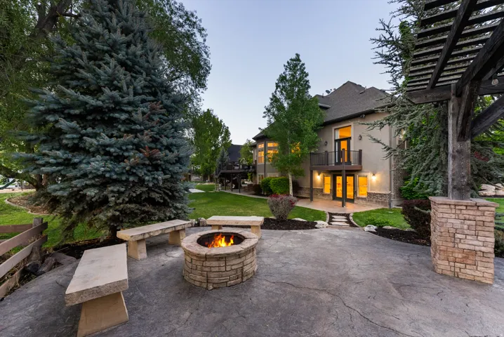 Stained concrete patio featuring a stone fire pit, three stone benches, and a large pergola structure
