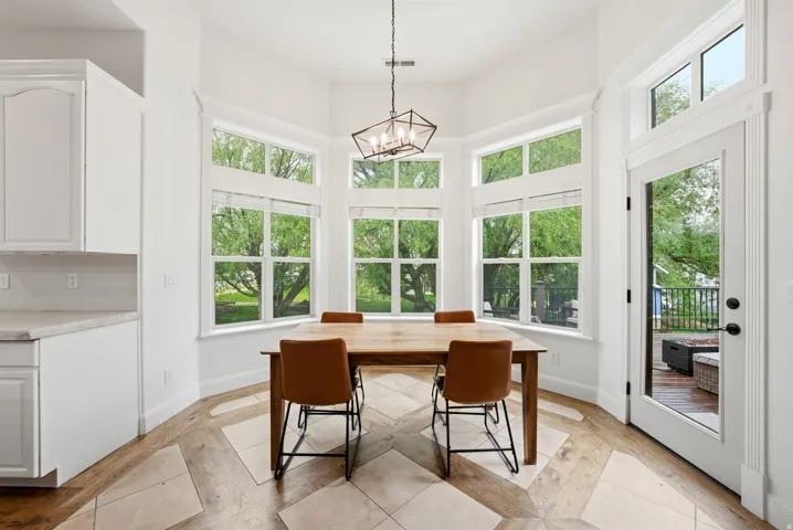 Bay window dining area with pattern wood-finish flooring, white cabinetry, light-toned countertop, and outdoor deck access