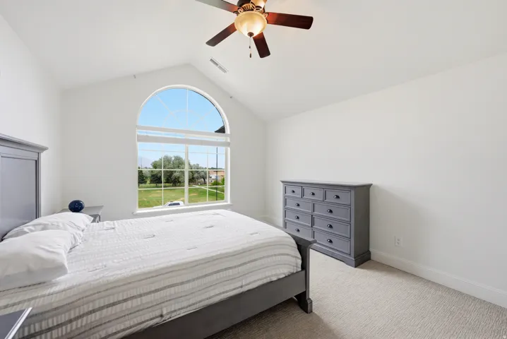 Vaulted ceiling with an arched window, ceiling fan with integrated lighting, and neutral tone carpeting