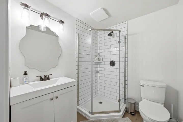 Bathroom featuring a glass-enclosed shower with subway tile surround, white vanity with integrated sink, decorative framed mirror, and wood-finish flooring