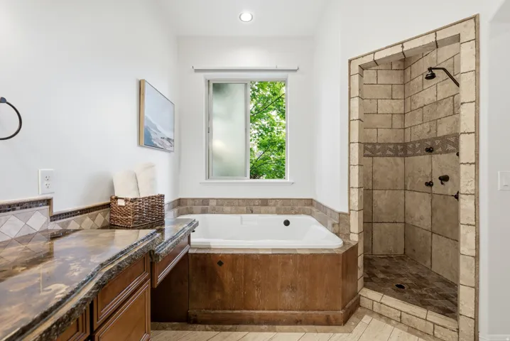 Full bathroom featuring an alcove shower with stone tile, a built-in soaking tub, and a vanity with a stone countertop and wood cabinetry