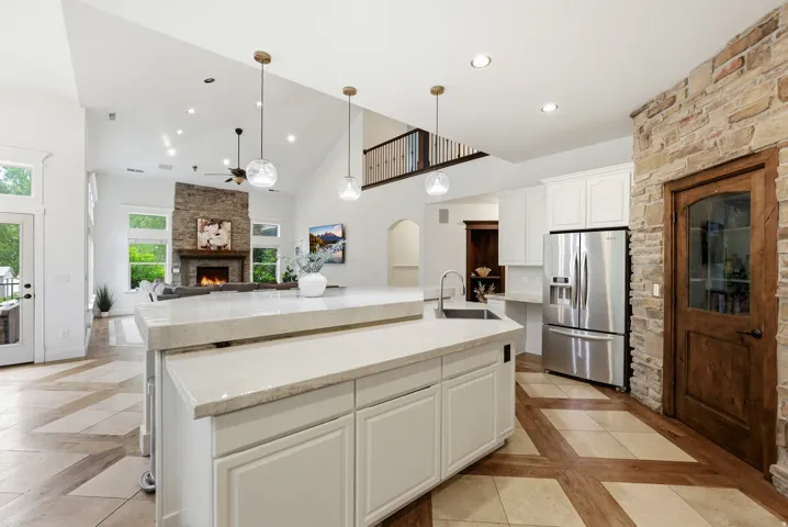 Open-concept kitchen featuring an island with a sink and pendant lighting, stainless steel refrigerator, white cabinetry, and stone-clad accent wall