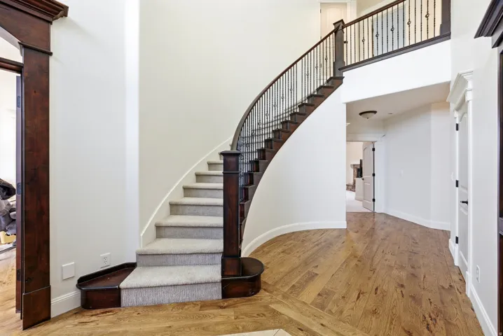 Grand curved staircase featuring dark wood newel posts and railings with decorative metal balusters