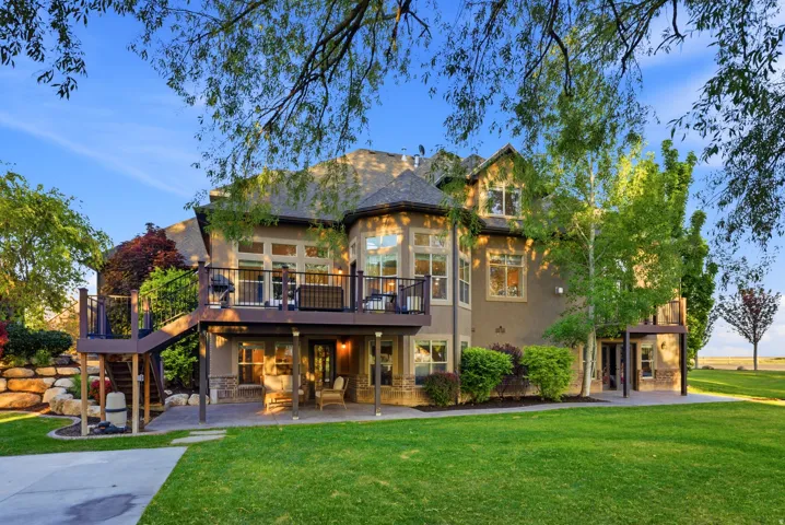 Spacious backyard featuring an elevated composite deck with black railings, a stone retaining wall, and a covered patio area